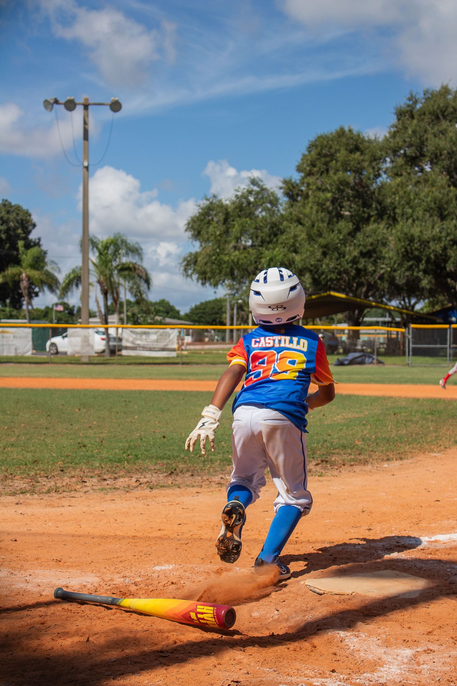 Baseball player stepping on base while running in bright blue uniform during game.