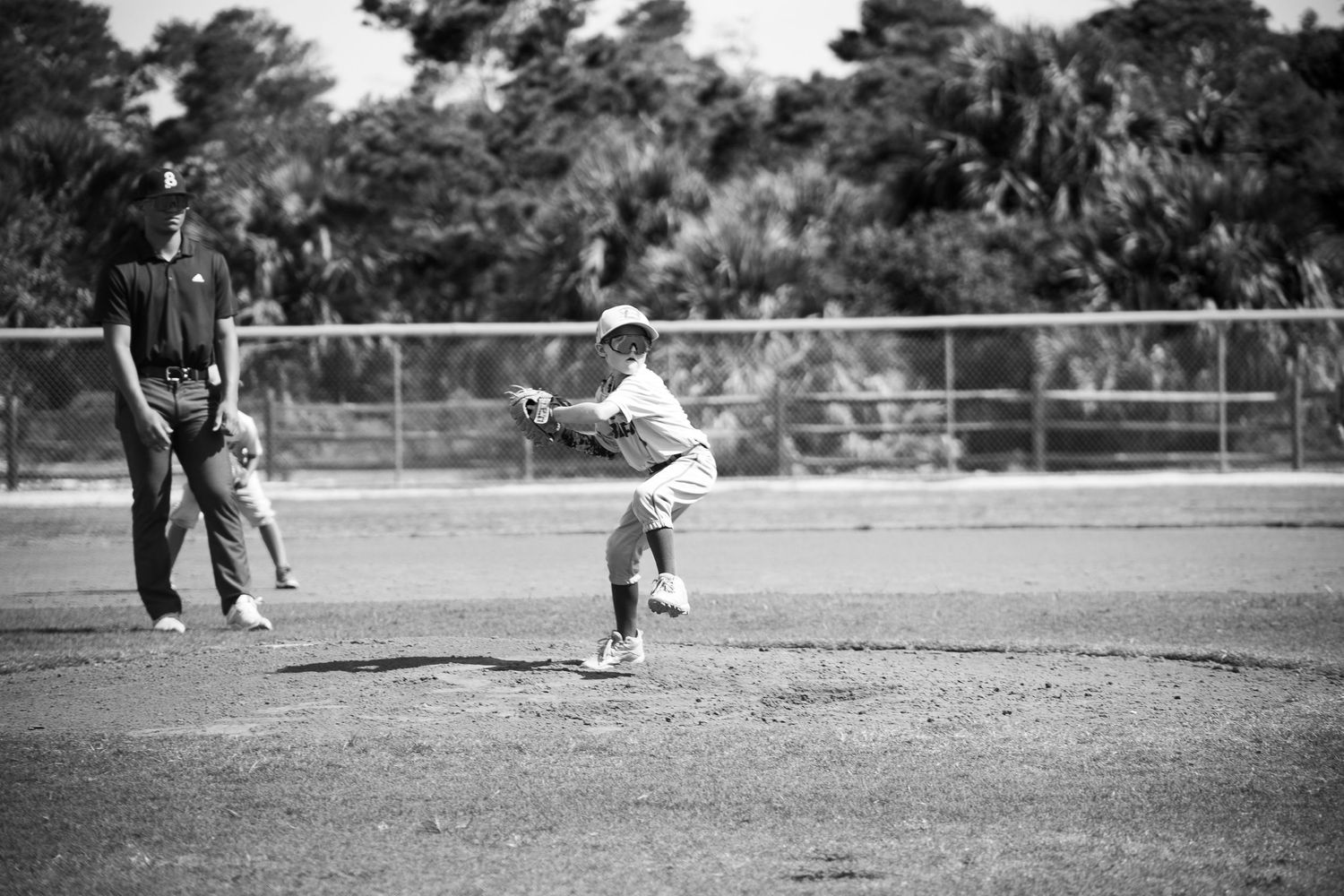 Black and white photo of baseball pitcher mid-throw on outdoor field.