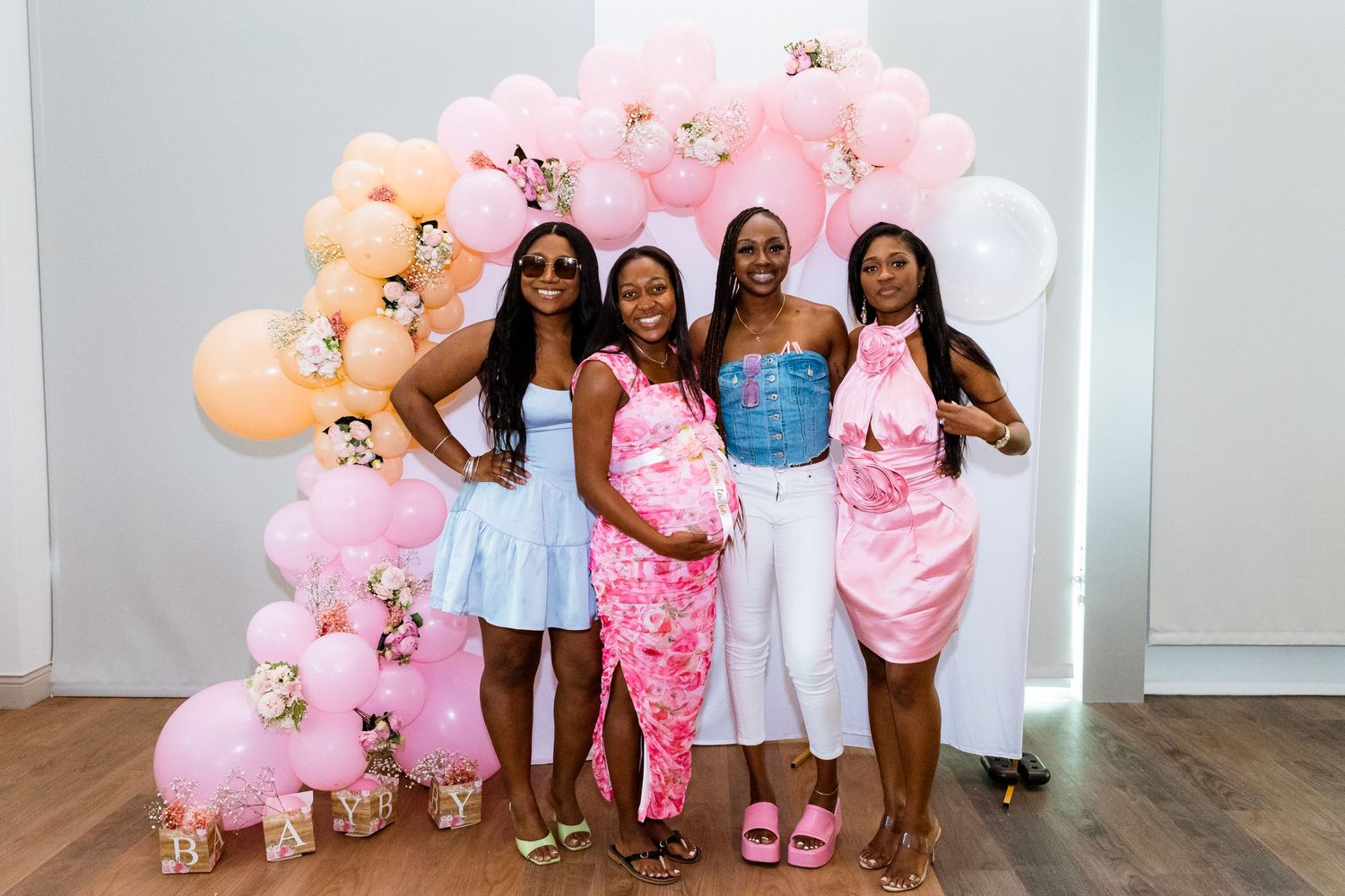 Group poses in front of pink and peach balloon arch at baby shower celebration.