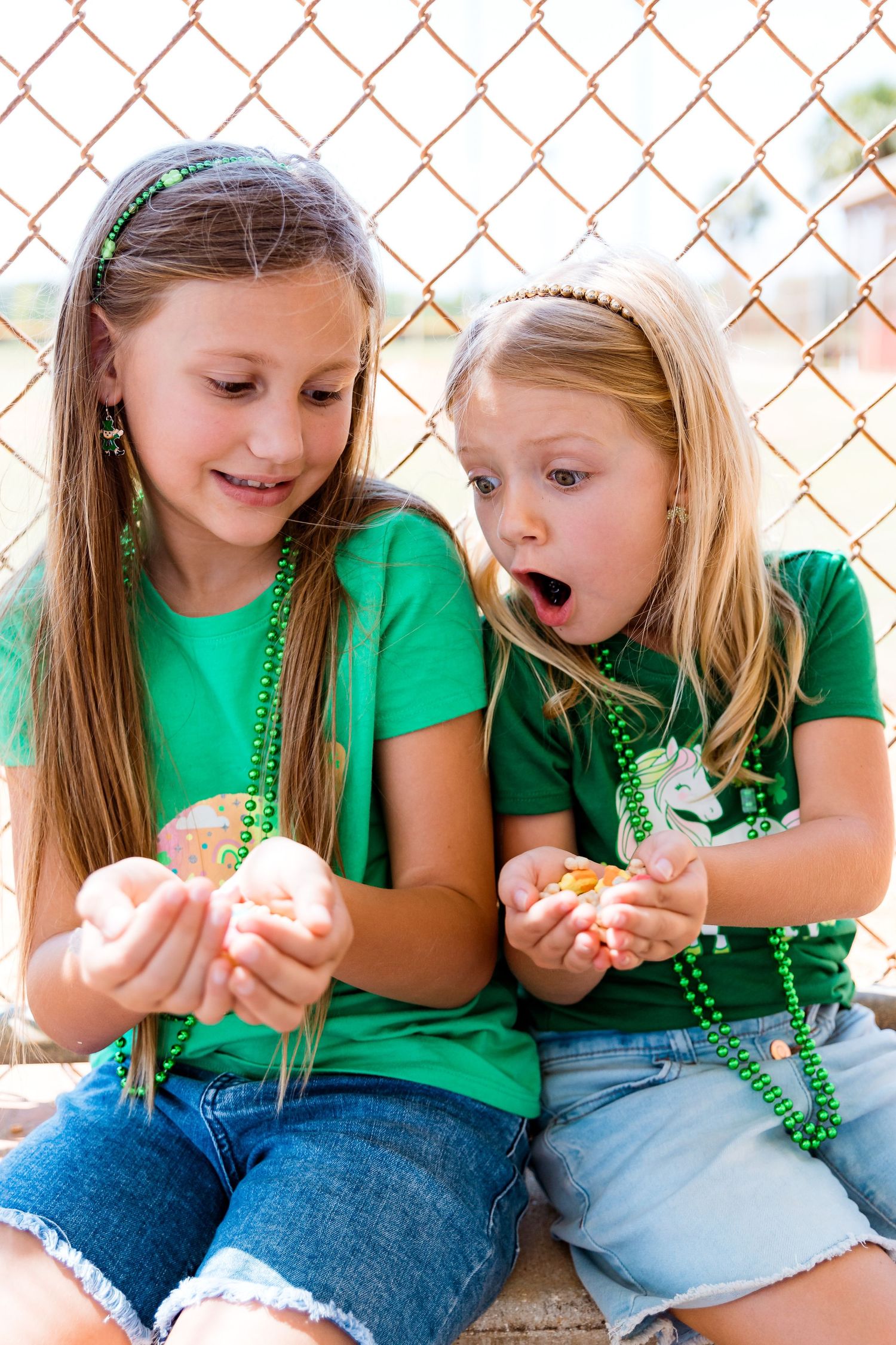 Children examining something in their hands while wearing green shirts and beaded necklaces.