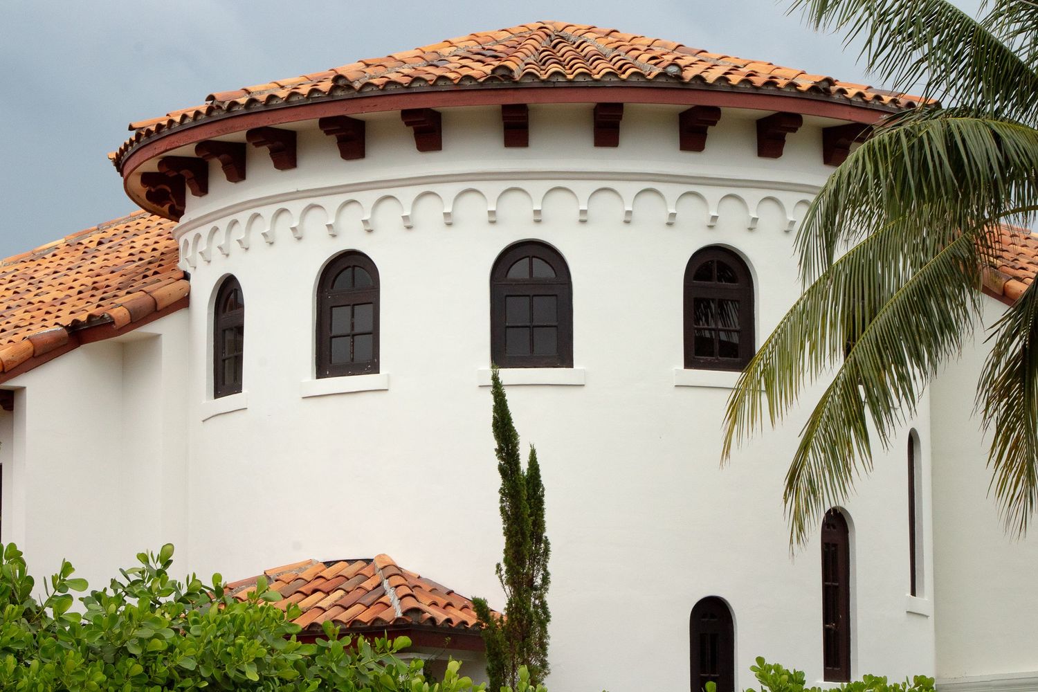 Spanish Mediterranean style architecture with white stucco walls, terracotta tile roof and arched windows framed by palm trees.