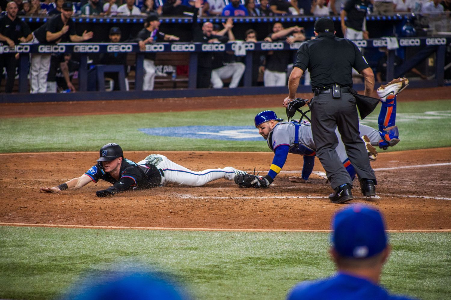 Baseball players in action near home plate during intense gameplay moment at night.