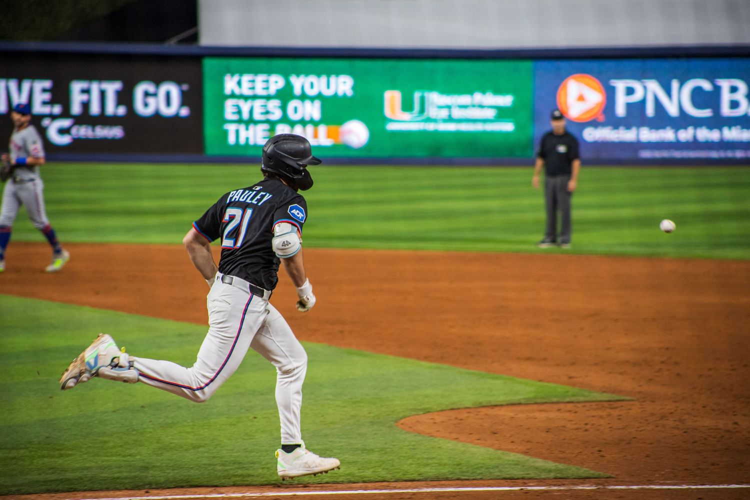 Baseball player in white uniform sprinting around the bases during a night game at a professional stadium.