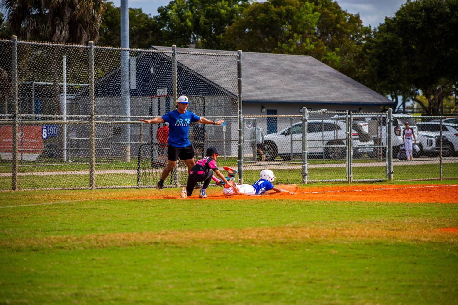 Baseball players compete on a grass field with orange clay infield during a sunny afternoon game.