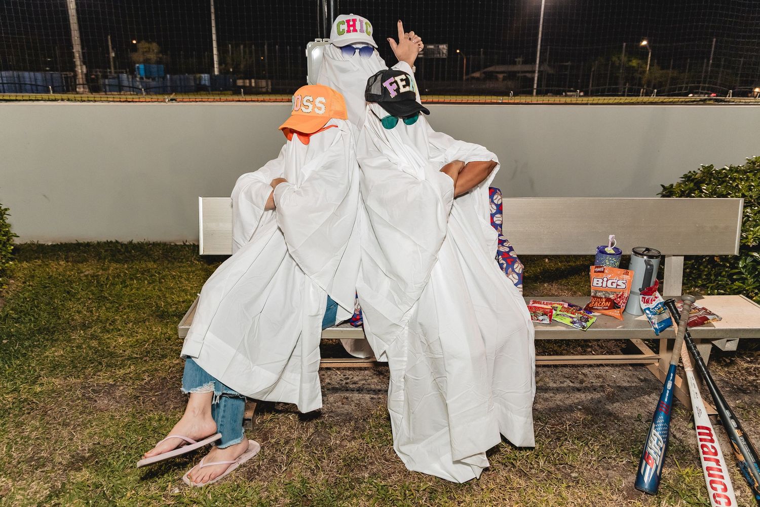 A group dressed in white ghost costumes plays on a sports field at night with glowing lights.