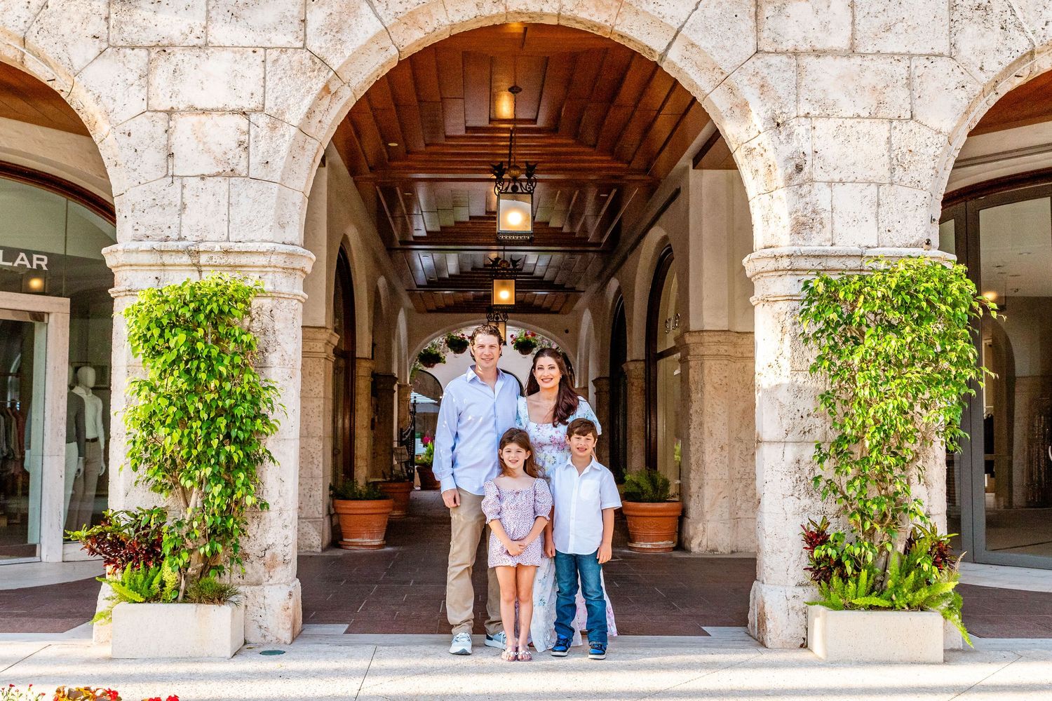 Family of four posing under stone archway at upscale outdoor shopping center.
