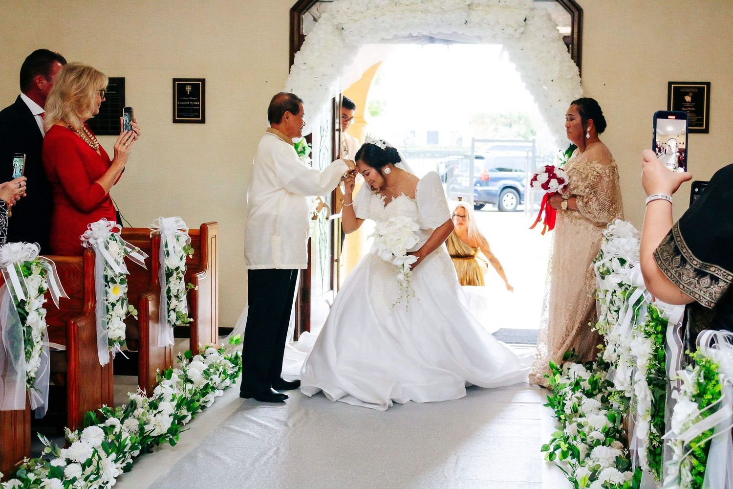 Wedding ceremony inside a small chapel with white flowers decorating the pews and aisle.