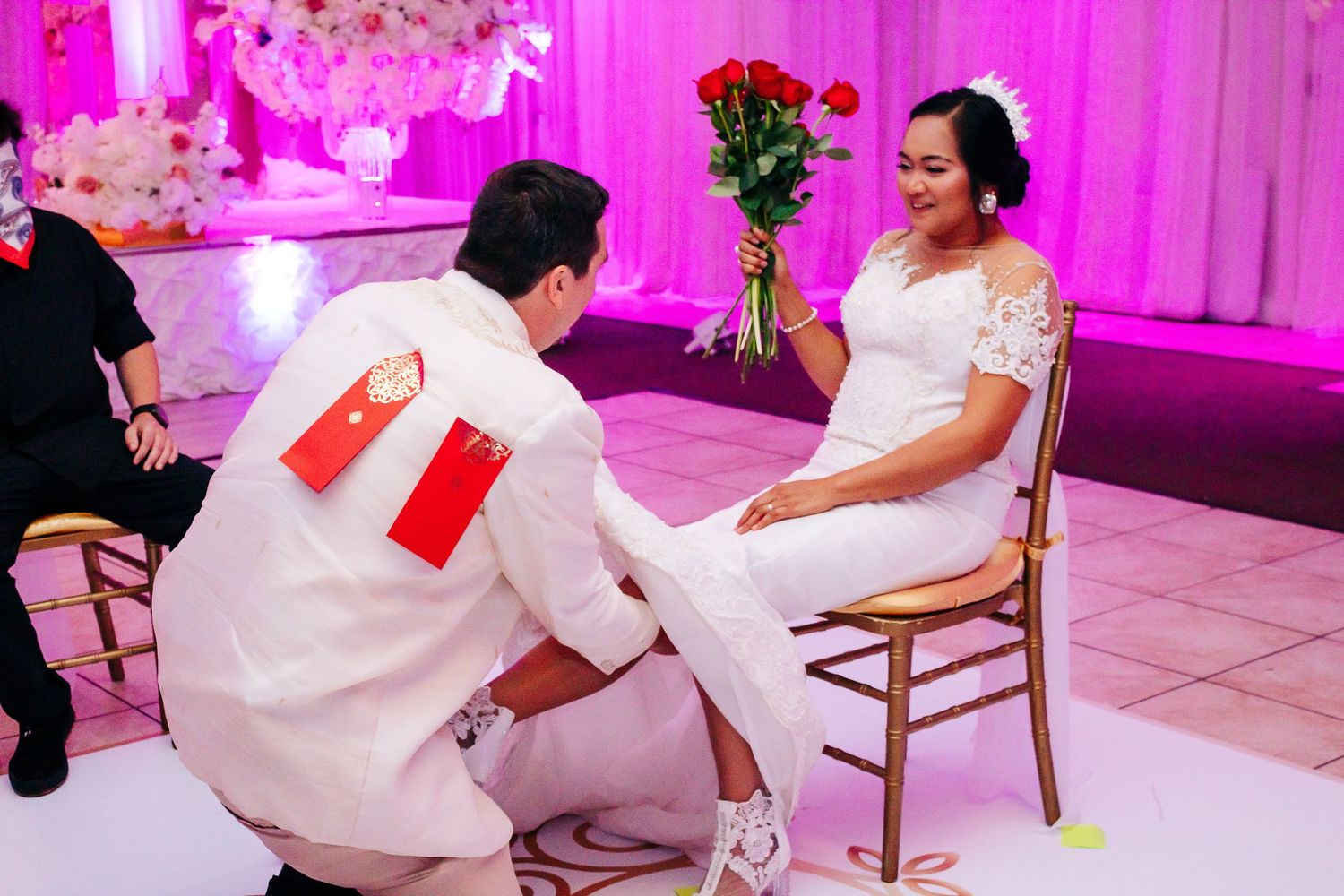 Wedding reception setup with pink flower arrangements and white decorative elements under vibrant magenta lighting.