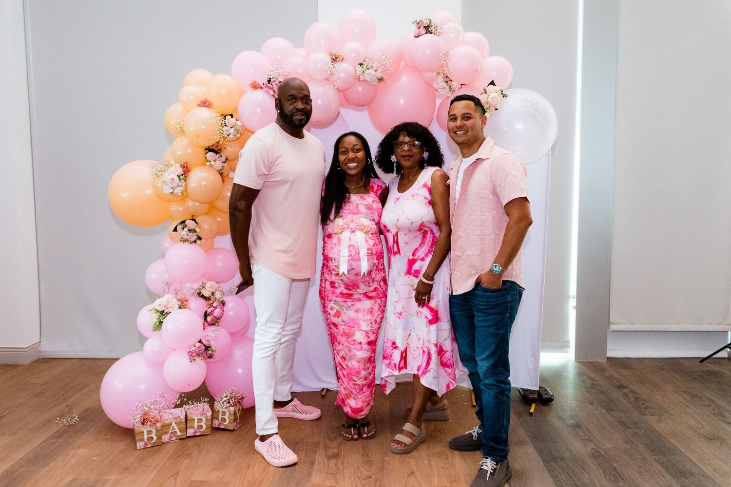 Friends and family gathered for a group photo at a pink-themed baby shower celebration.