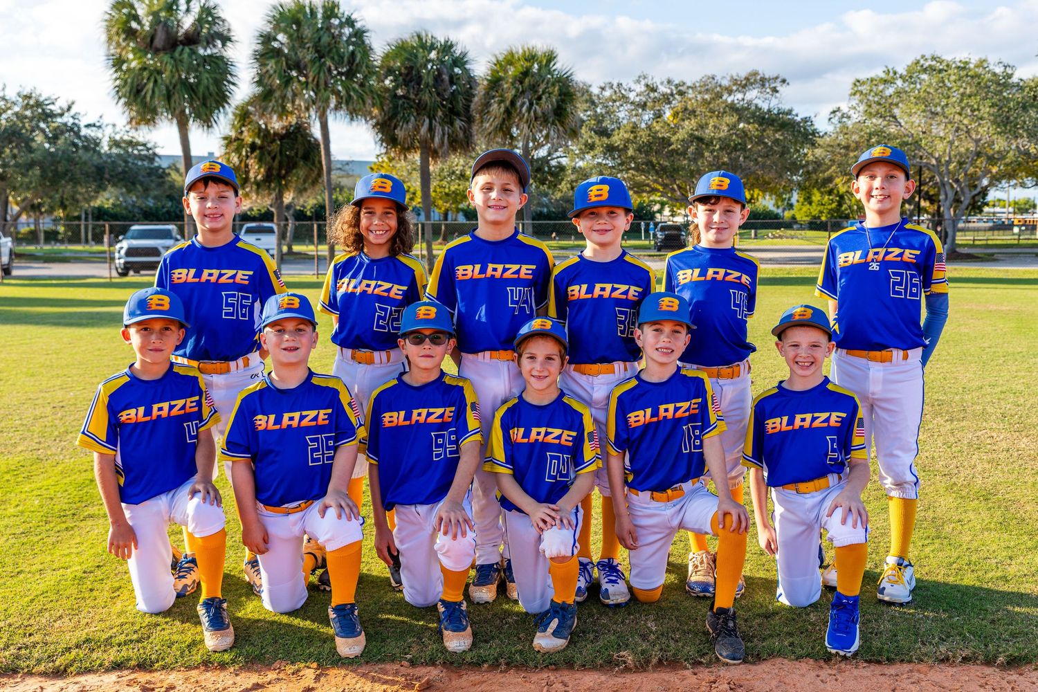 Youth baseball team in blue jerseys poses together on sunny field for team photo.