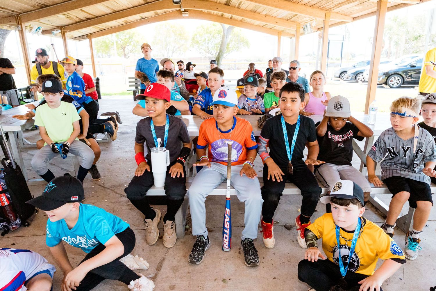 A group of sports players rests on benches under a covered shelter during a daytime sports event.