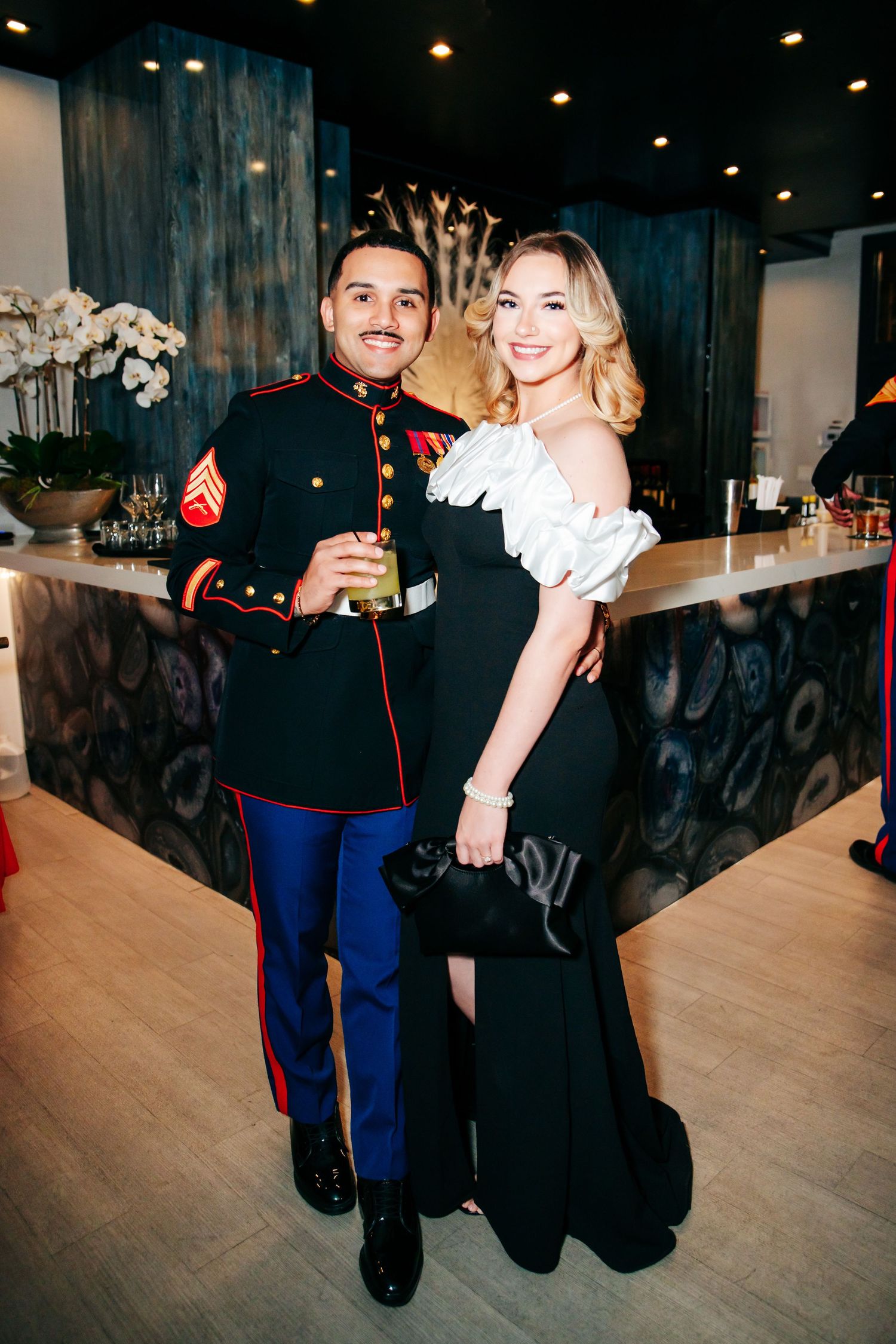 People in formal attire including military dress uniforms gather at an evening celebration.