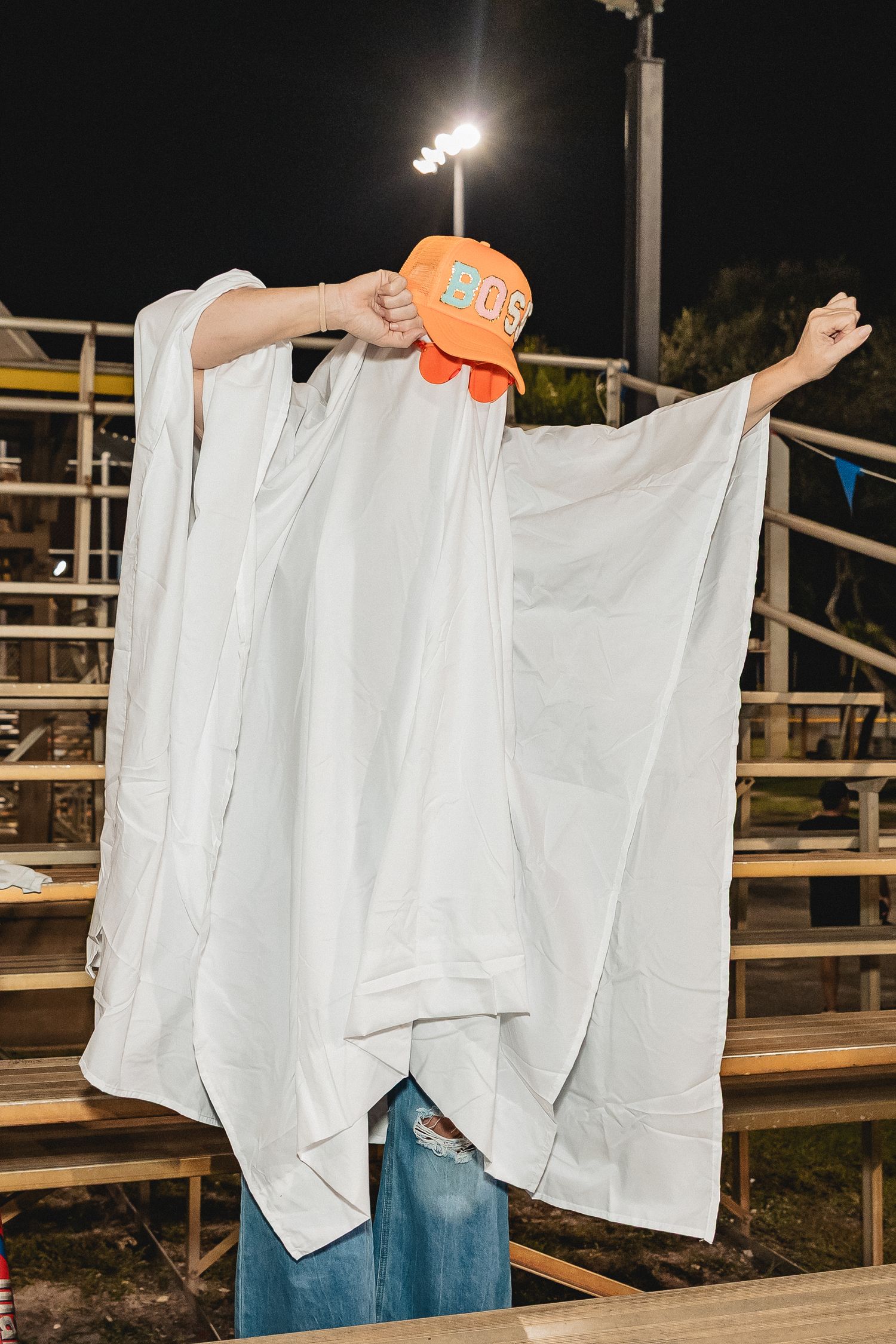 People wearing white sheets perform a wave motion in bleachers at a nighttime event.