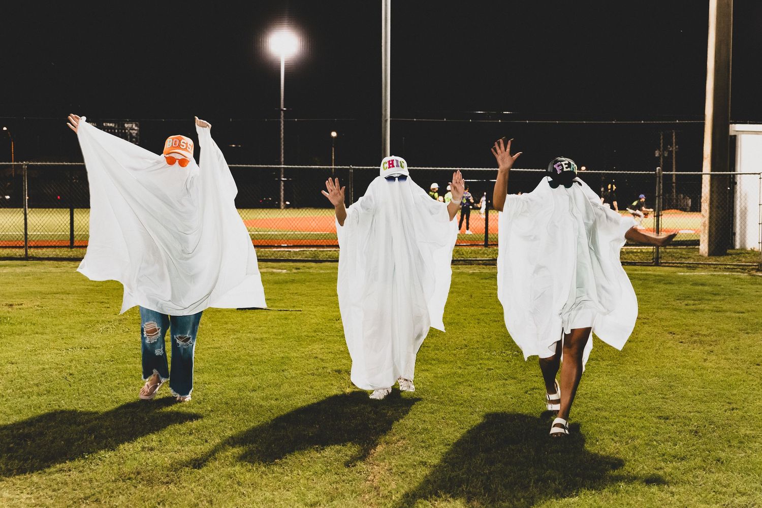 People in white ghost costumes play and pose on a grassy field at night.