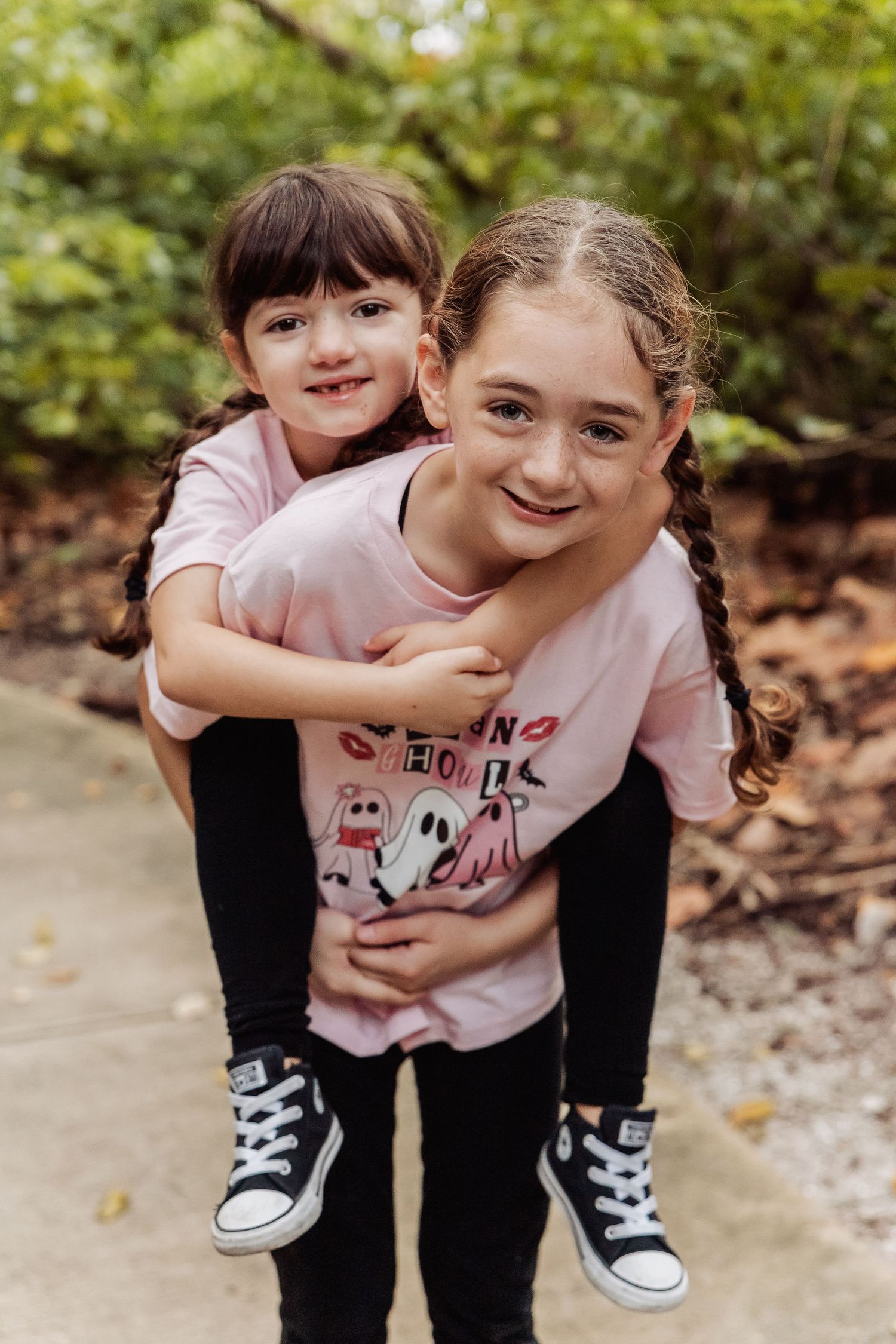 A playful piggyback ride sequence showing black pants and classic Converse sneakers against a natural outdoor backdrop.