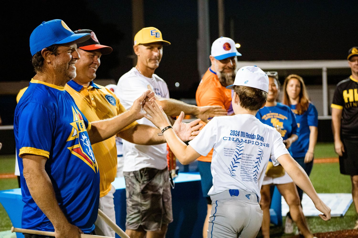 Baseball players and coaches interact during a team gathering wearing blue and yellow uniforms.