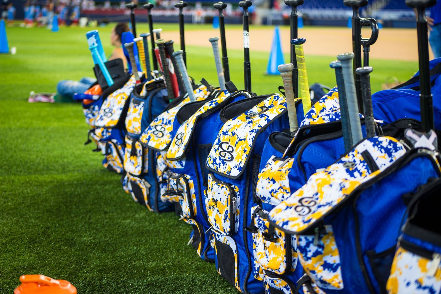 Row of blue and yellow baseball equipment bags lined up on green turf field.