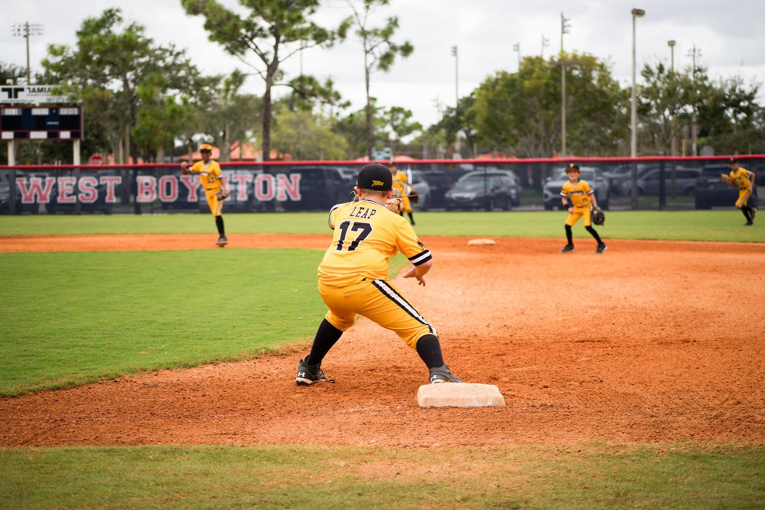 Baseball player in yellow uniform leads off from first base during game on well-maintained field.
