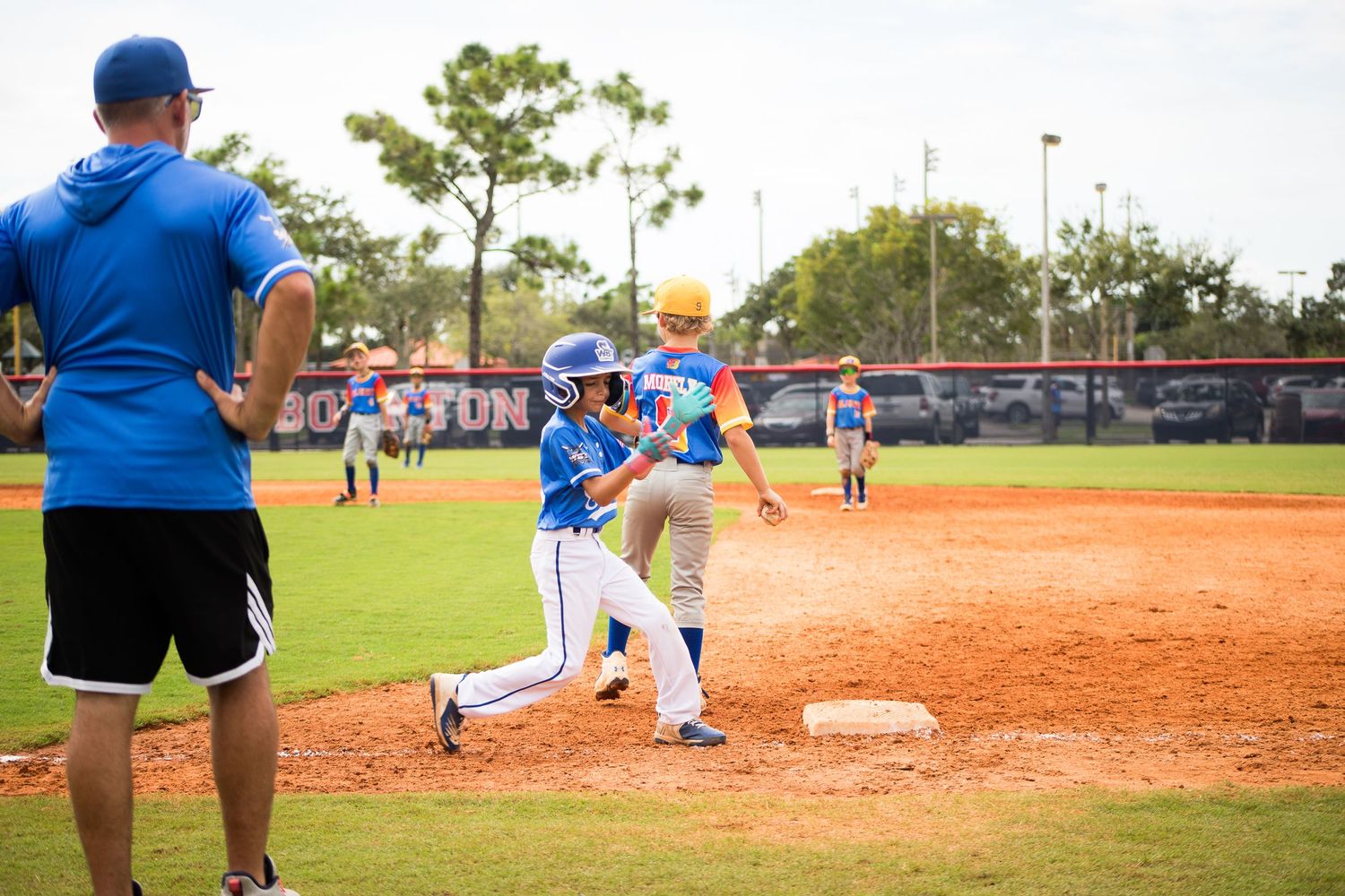 Baseball player practicing base running while coach observes on dirt infield.