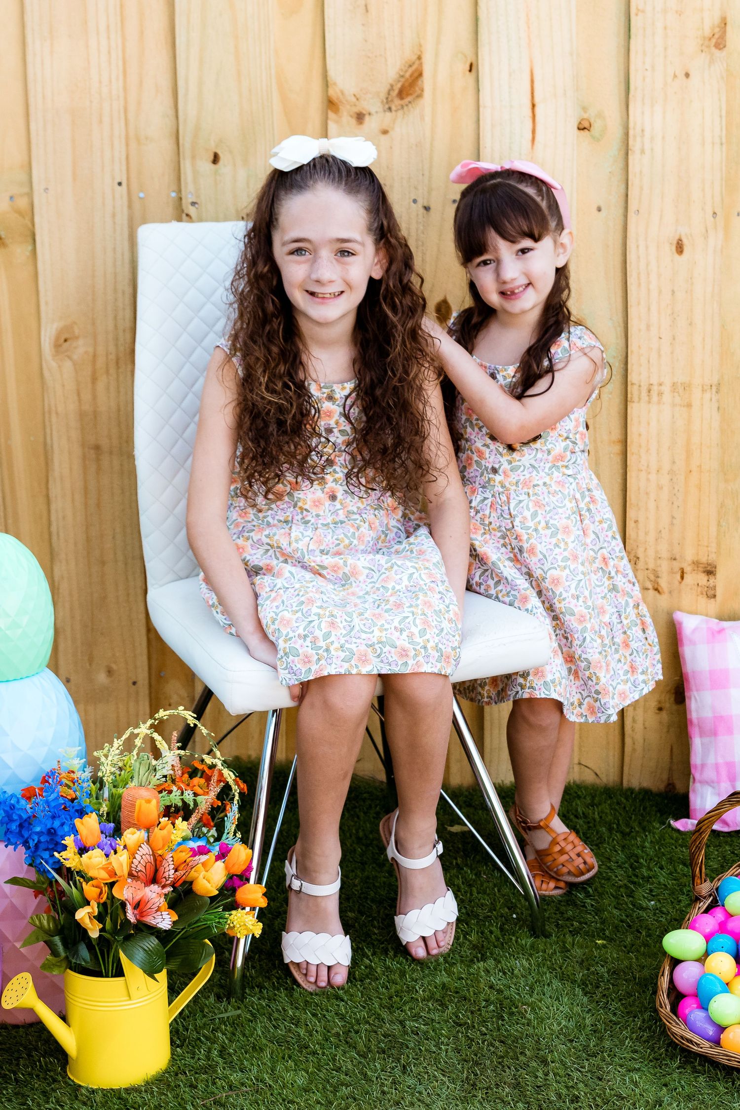 Children in floral dresses pose together near Easter decorations and spring flowers.