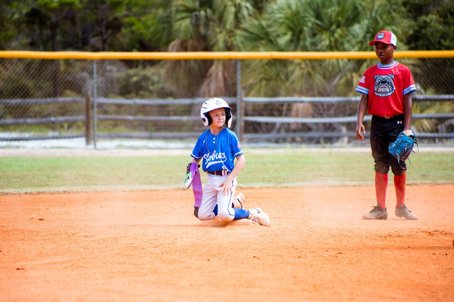 Baseball game in progress on an orange clay field with players positioned strategically.