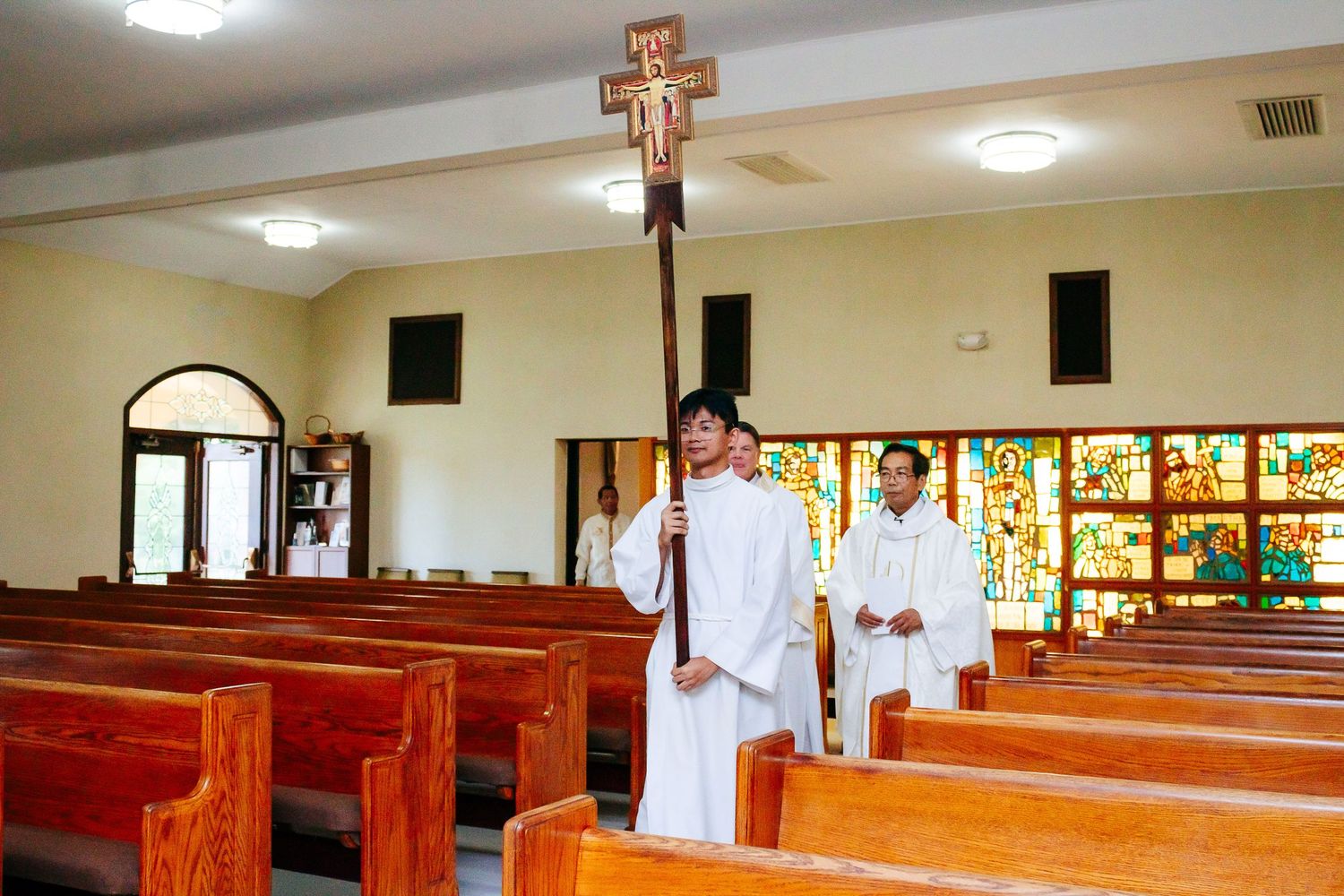 Long rows of wooden pews inside a church sanctuary with stained glass windows.