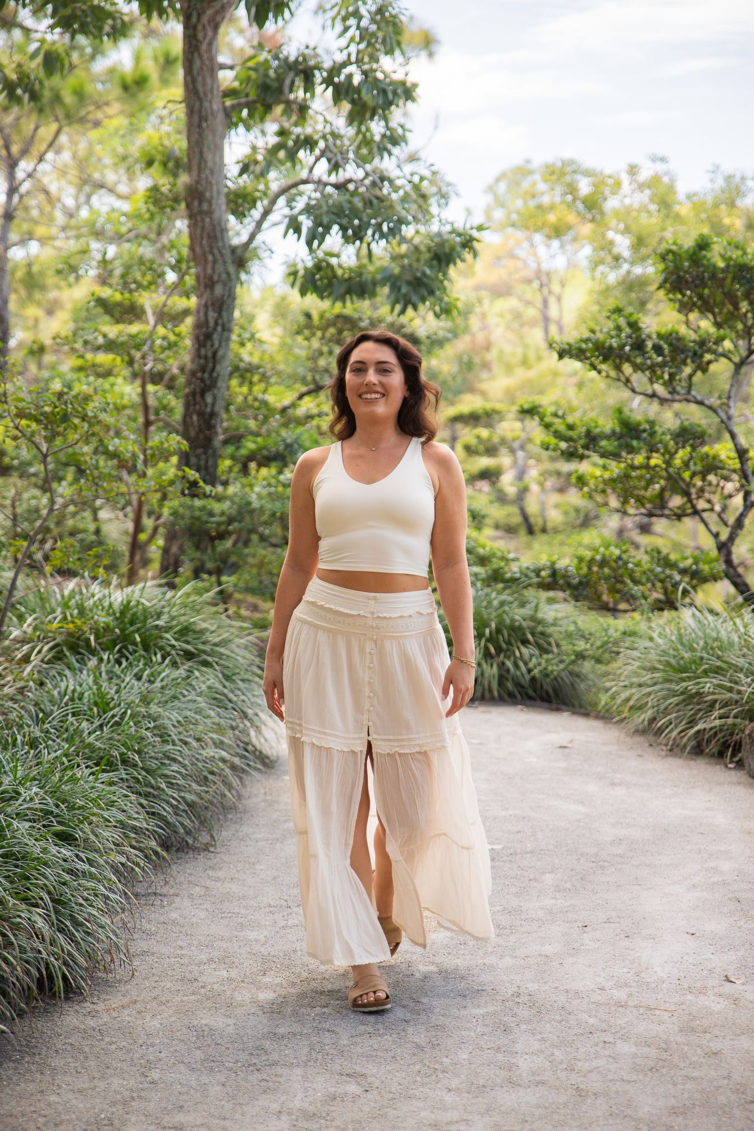 A series of four photos showing someone wearing a flowing cream-colored summer dress walking along a garden path surrounded by trees.