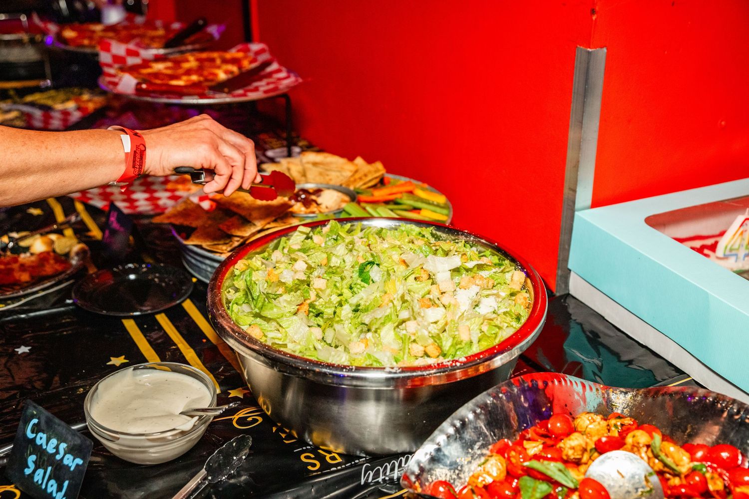 A close-up view of a large bowl filled with a creamy, green salad or dip, surrounded by various other dishes and plates of food on a table.