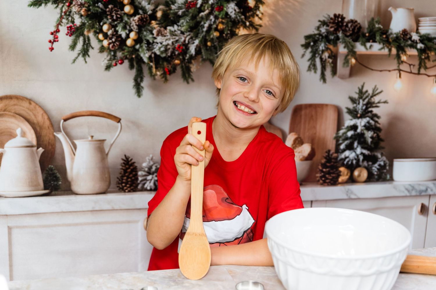 Person in red sweater smiling while decorating for Christmas with garland and festive decor in bright kitchen.