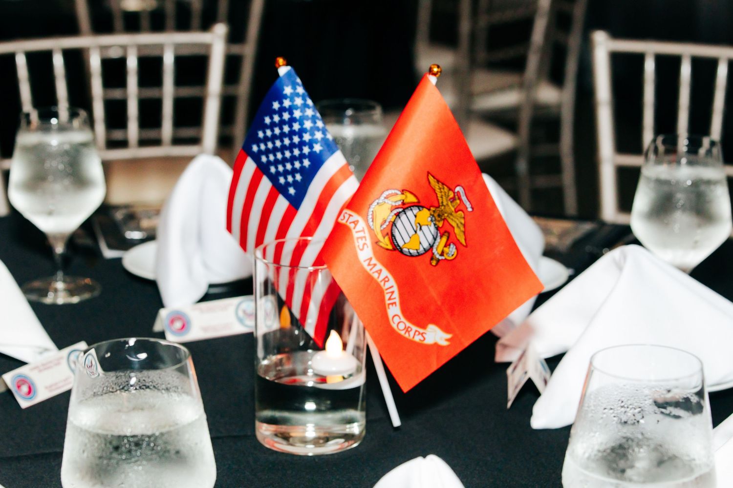 Table settings with American and Marine Corps flags displayed alongside water glasses at a formal dinner.