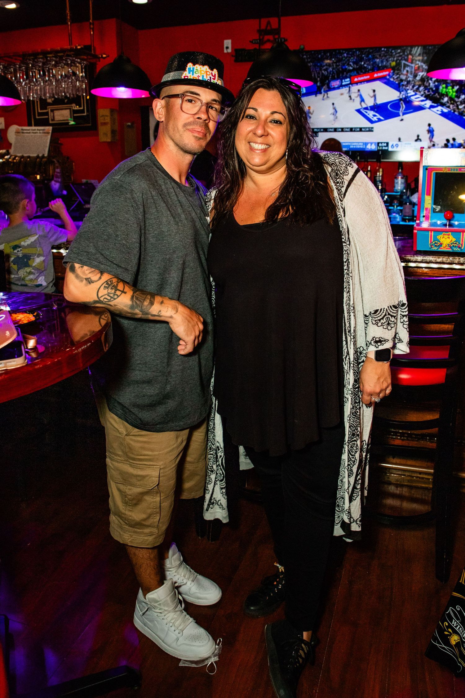 A man and a woman posing for a photo in a bar with arcade games.