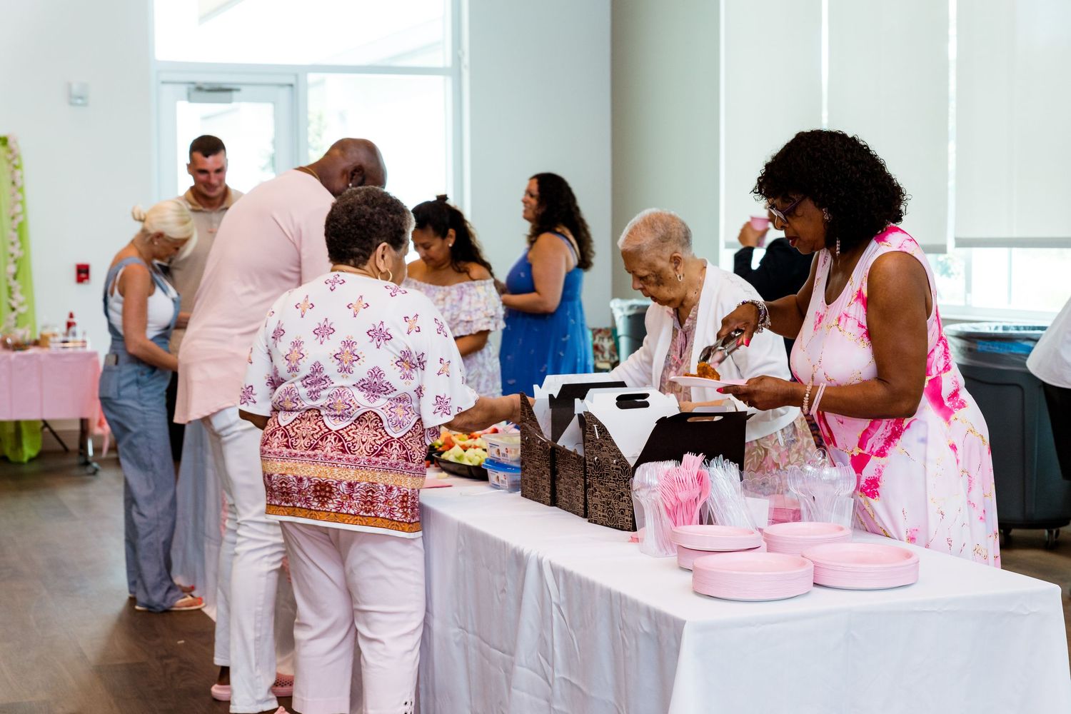 Guests gather around a buffet table with pink decorations at a festive celebration event.