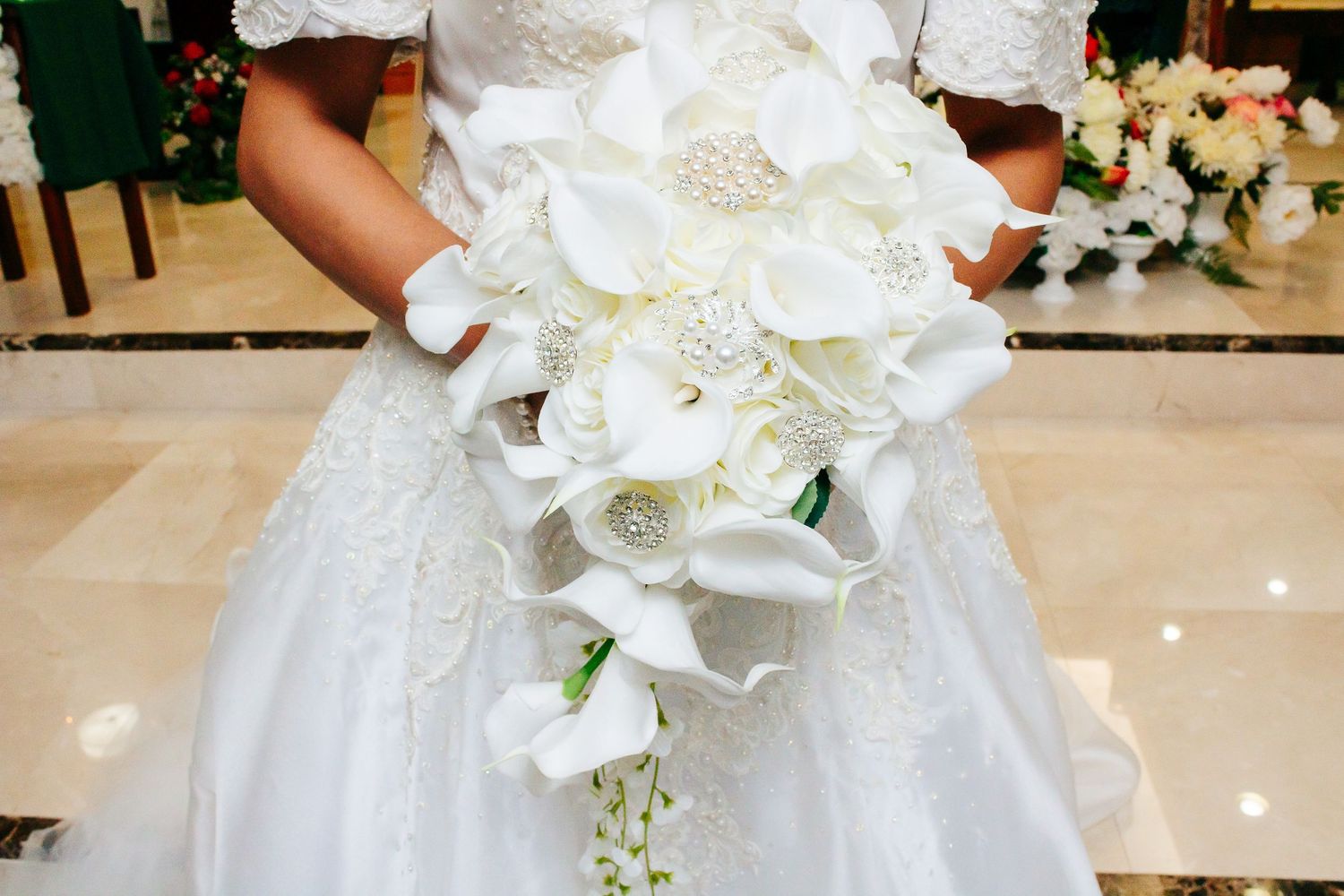 Elegant white wedding bouquet with orchids and lilies held against a formal dress.