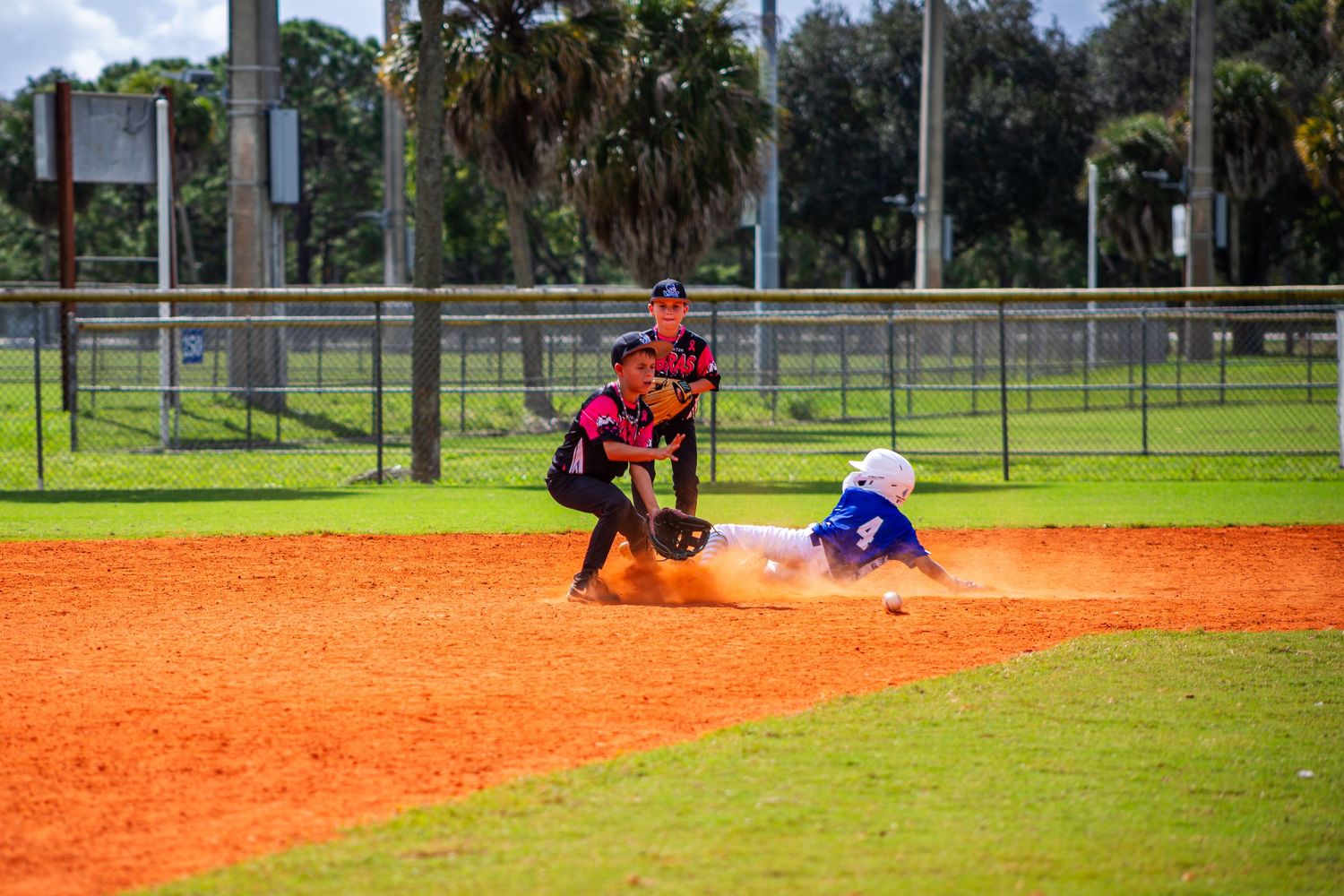 Baseball player in blue jersey slides into base while fielder in red uniform attempts to make the tag during game.