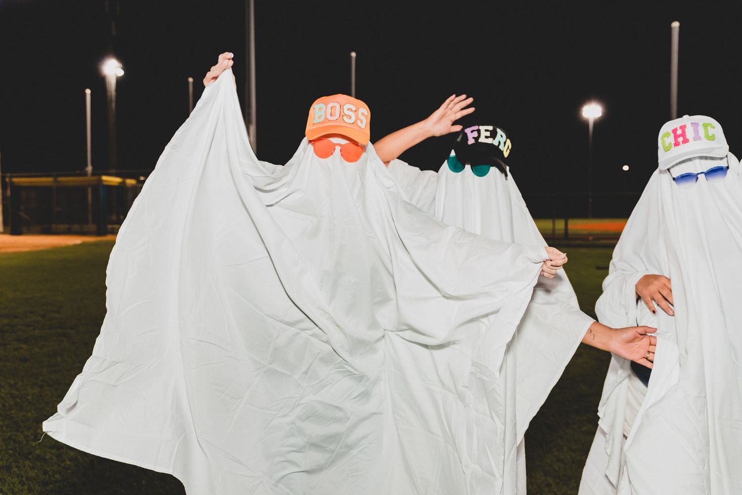People in white ghost costumes dance and play on a sports field under evening lights.
