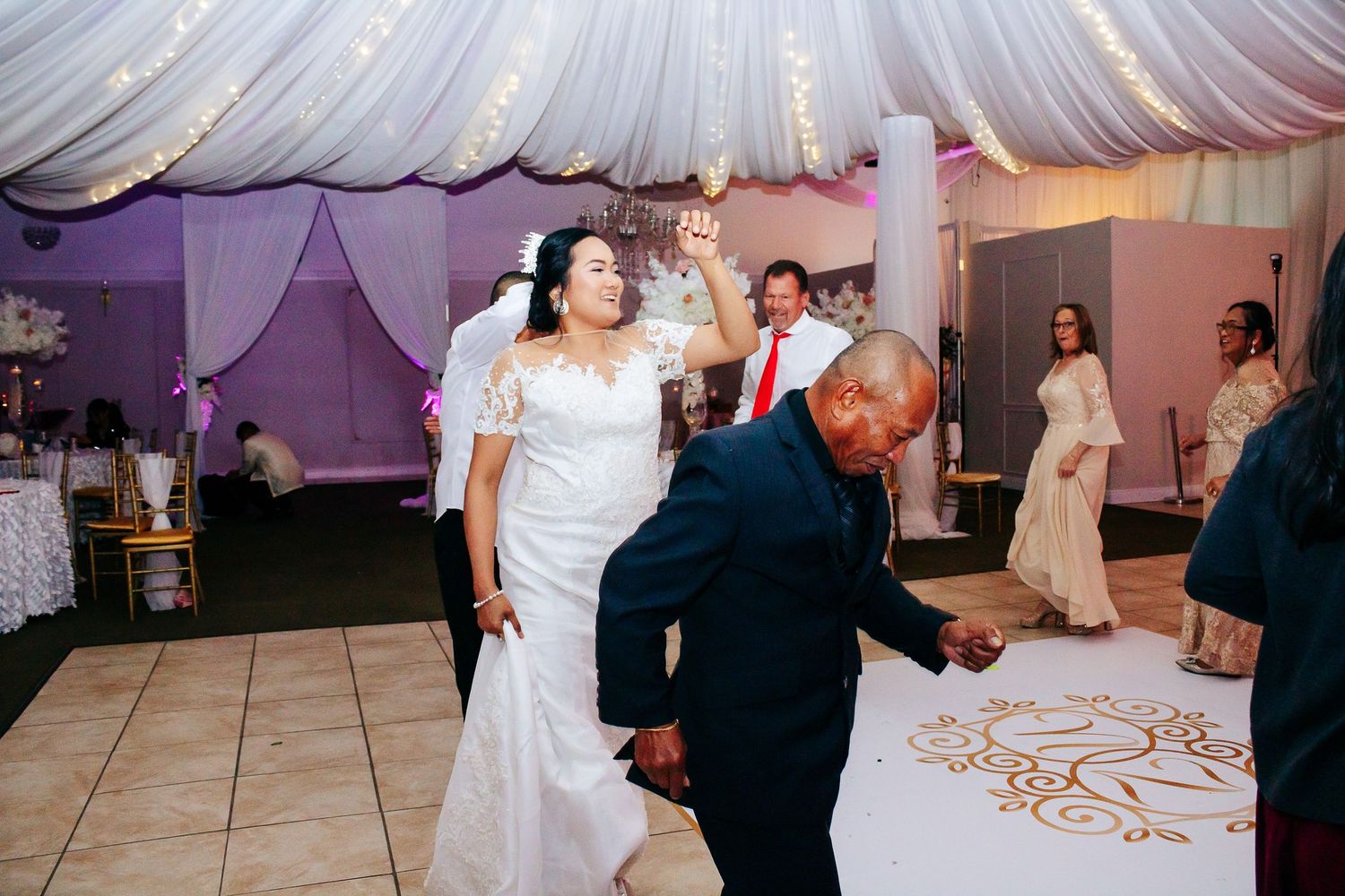 Wedding reception dance floor decorated with white fabric draping and purple lighting.