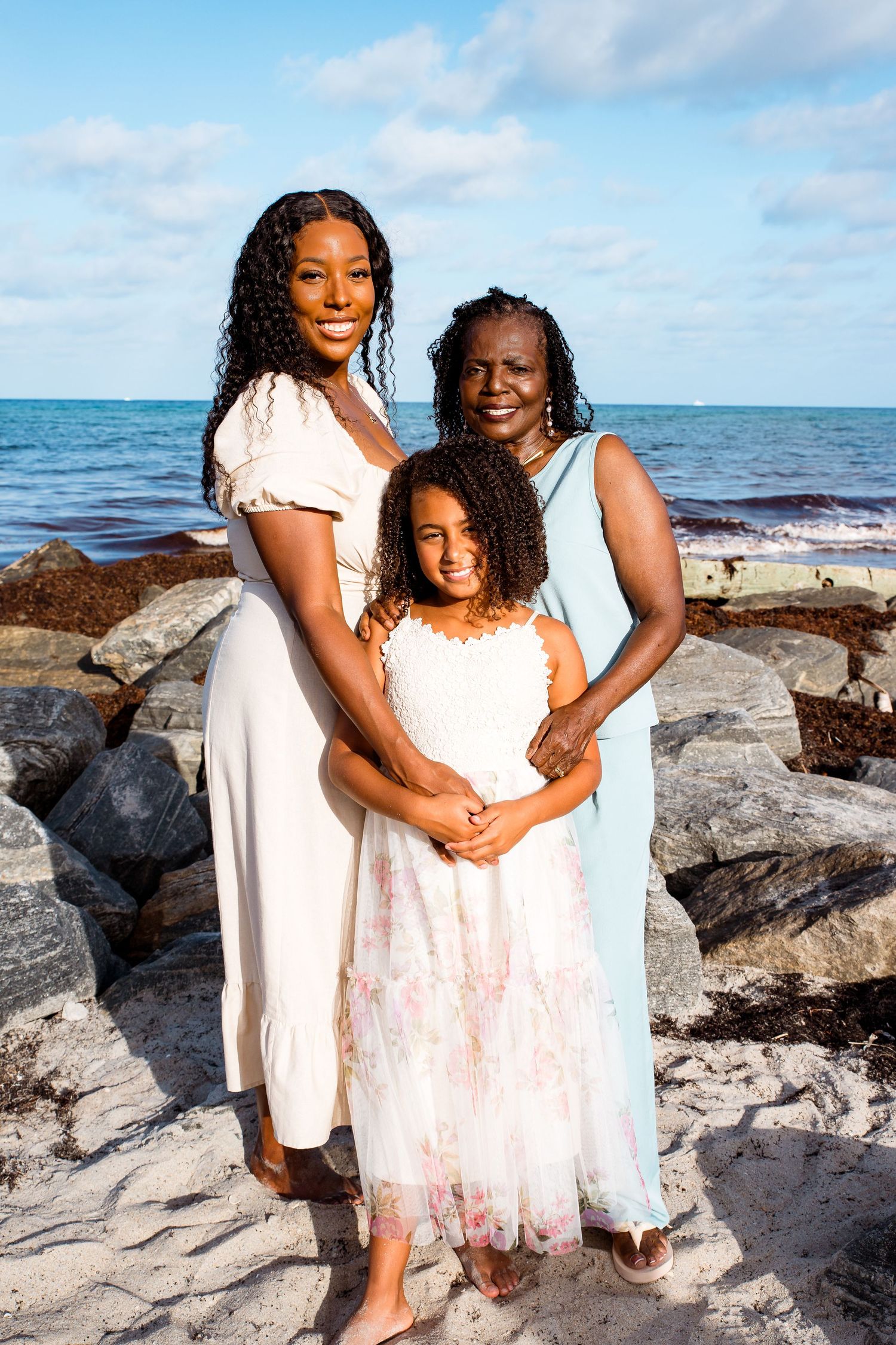 A loving family poses for photos while sitting on coastal rocks near the ocean on a sunny day.