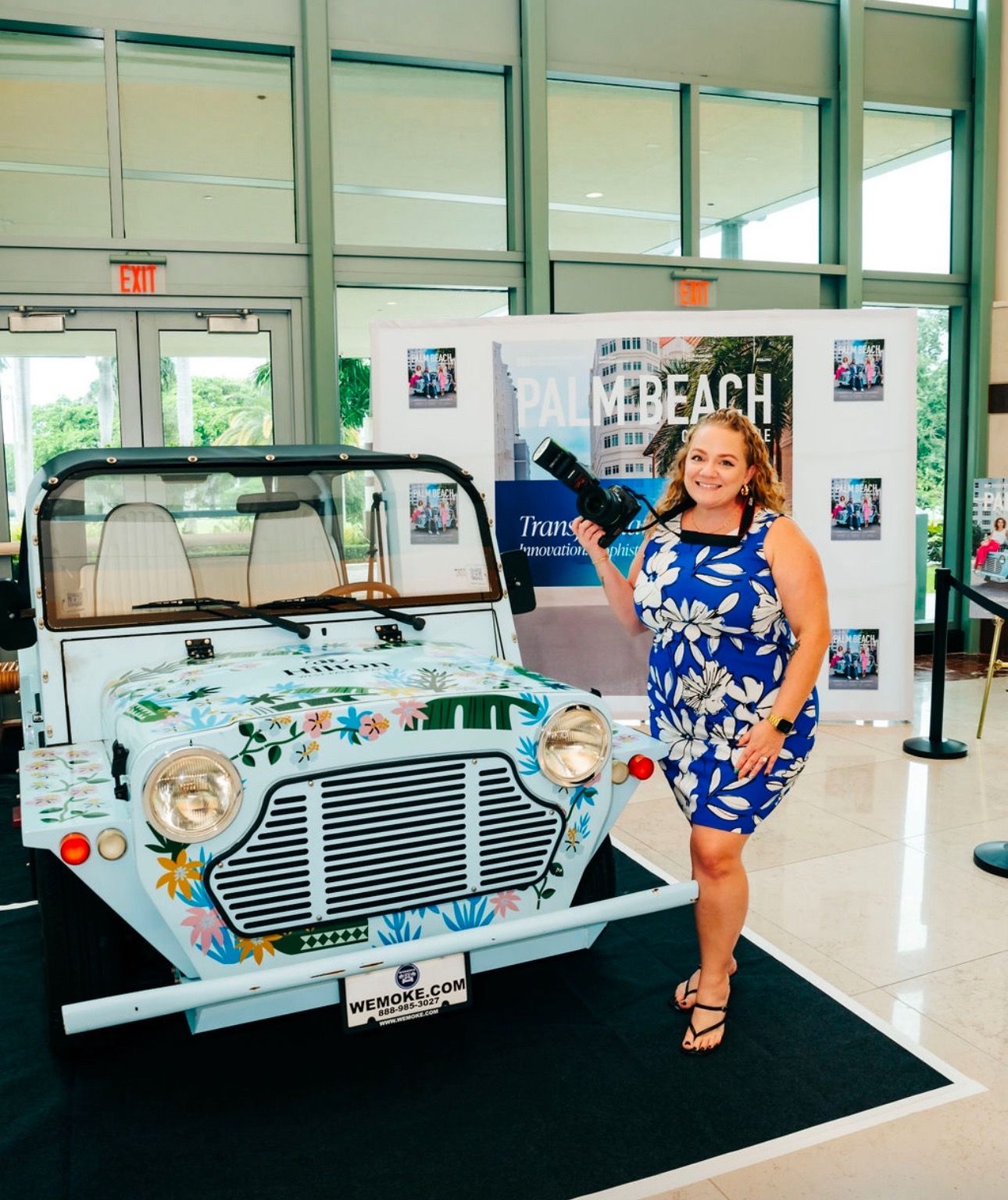 A vintage Mini Moke car decorated in blue and white patterns is displayed in a bright showroom setting.