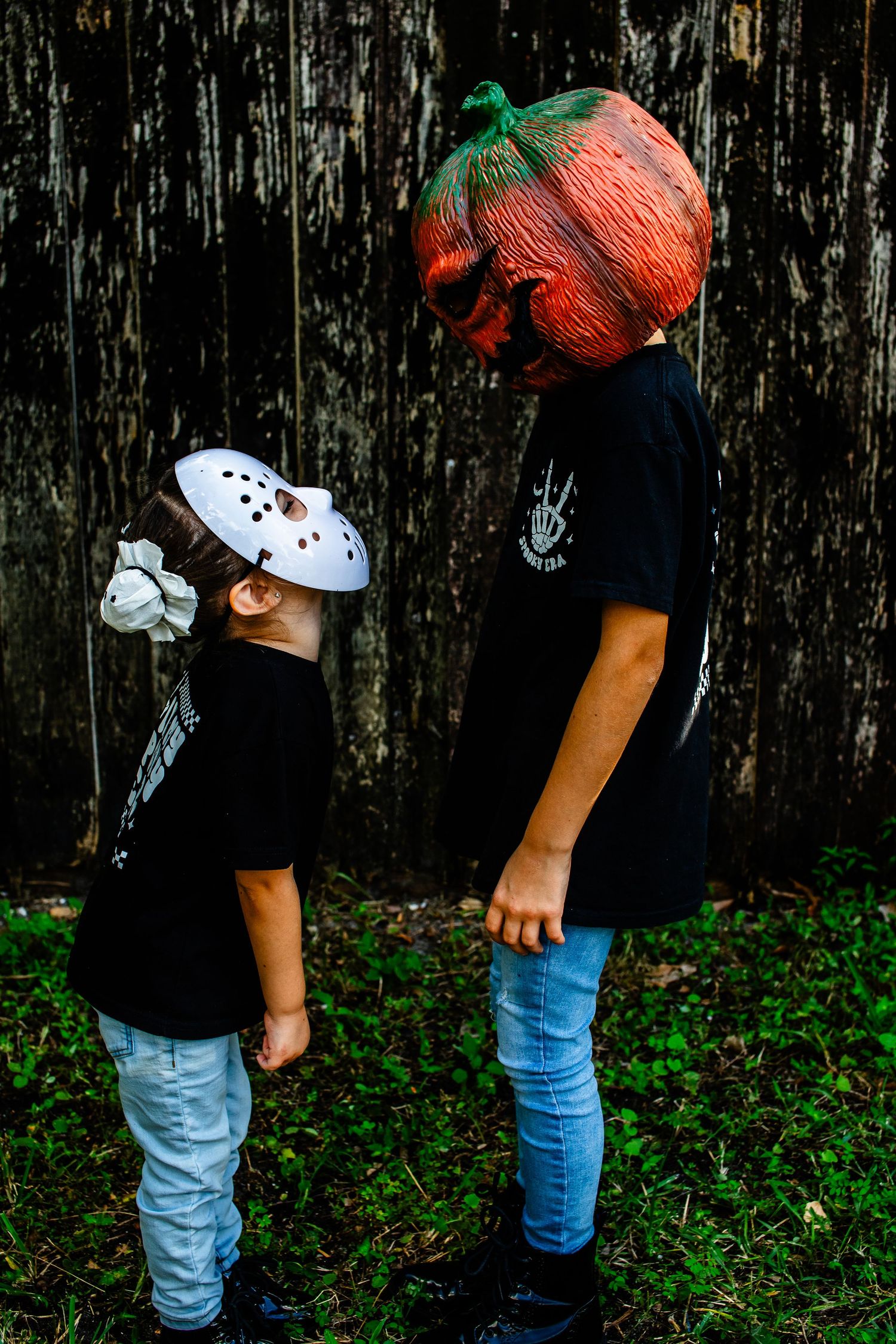 Two kids in spooky masks looking at each other against dark background.
