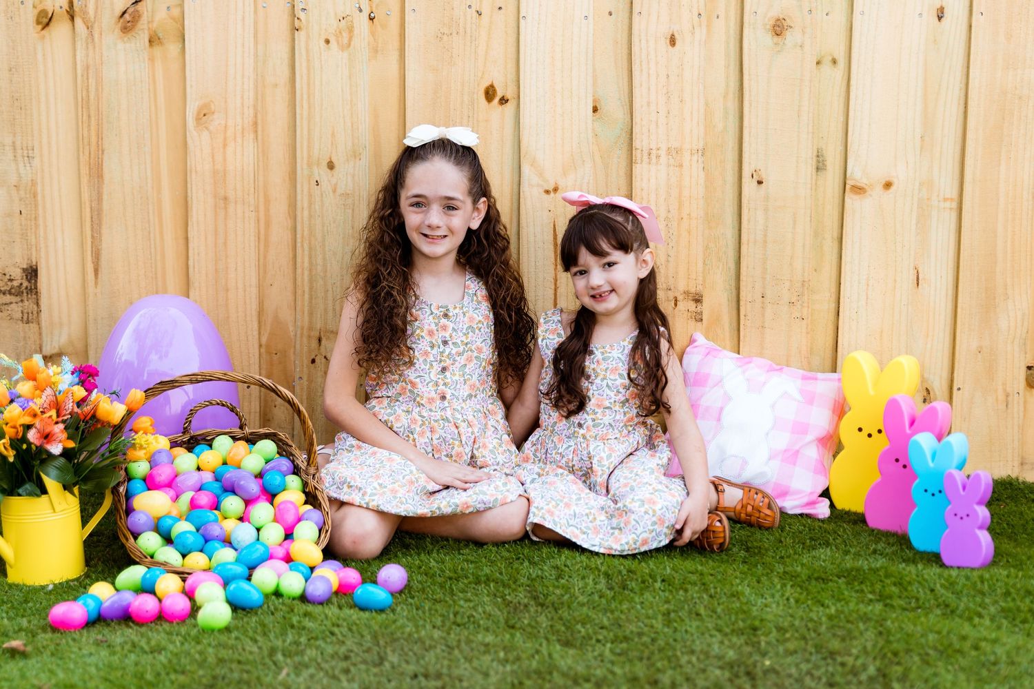 Easter photo setup with spring decor, colorful eggs, and floral dresses against a wooden fence backdrop.