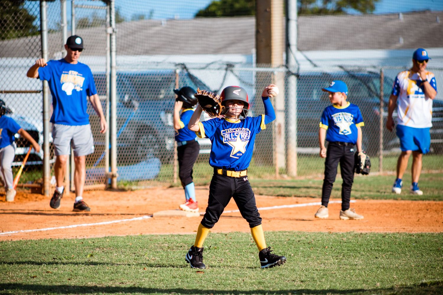 Young baseball player practicing batting stance while coaches observe during practice session.