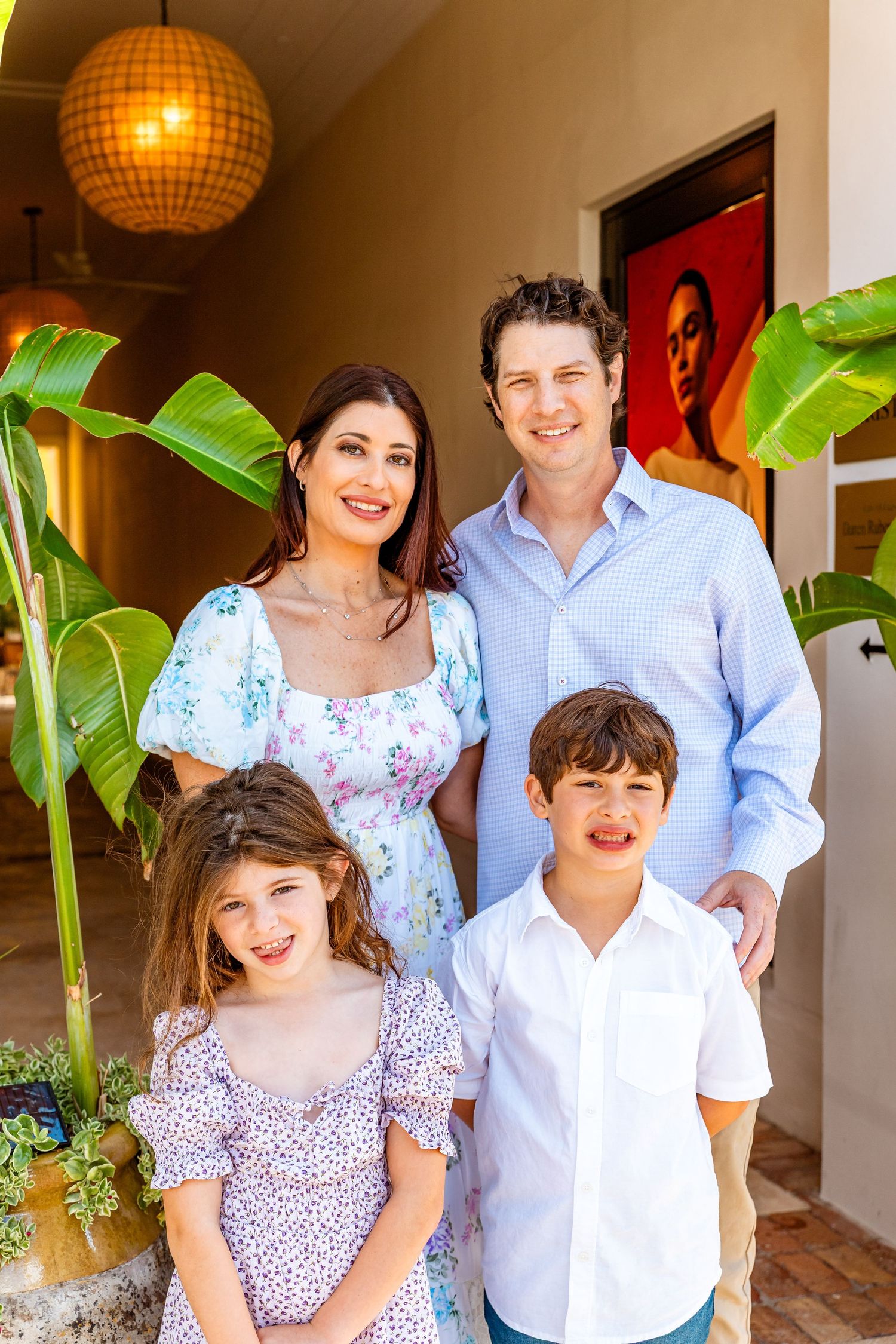 Happy family of four smiling together near tropical plants inside a bright, decorated home entrance.