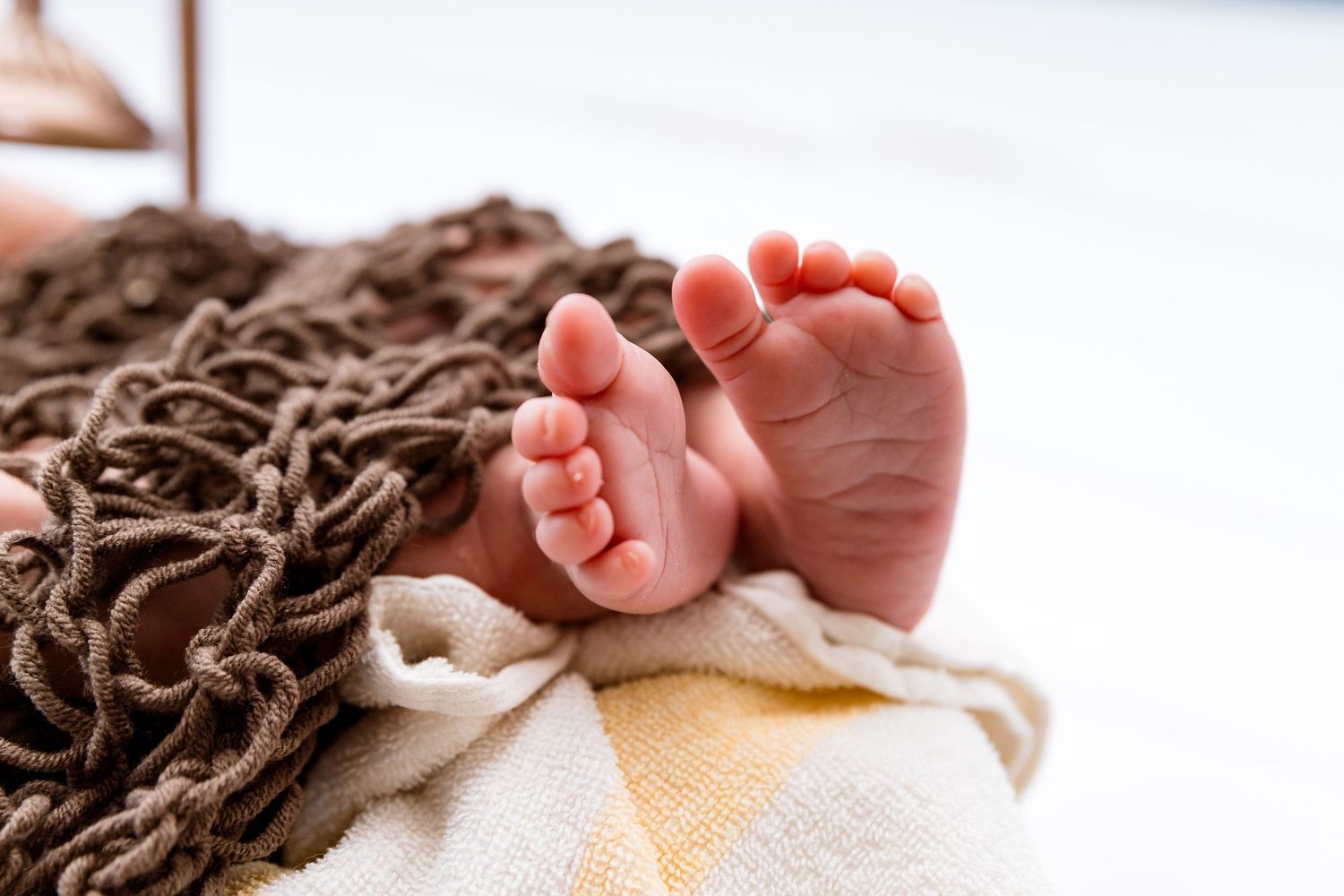 Close up of tiny newborn baby feet resting on brown textured blanket.