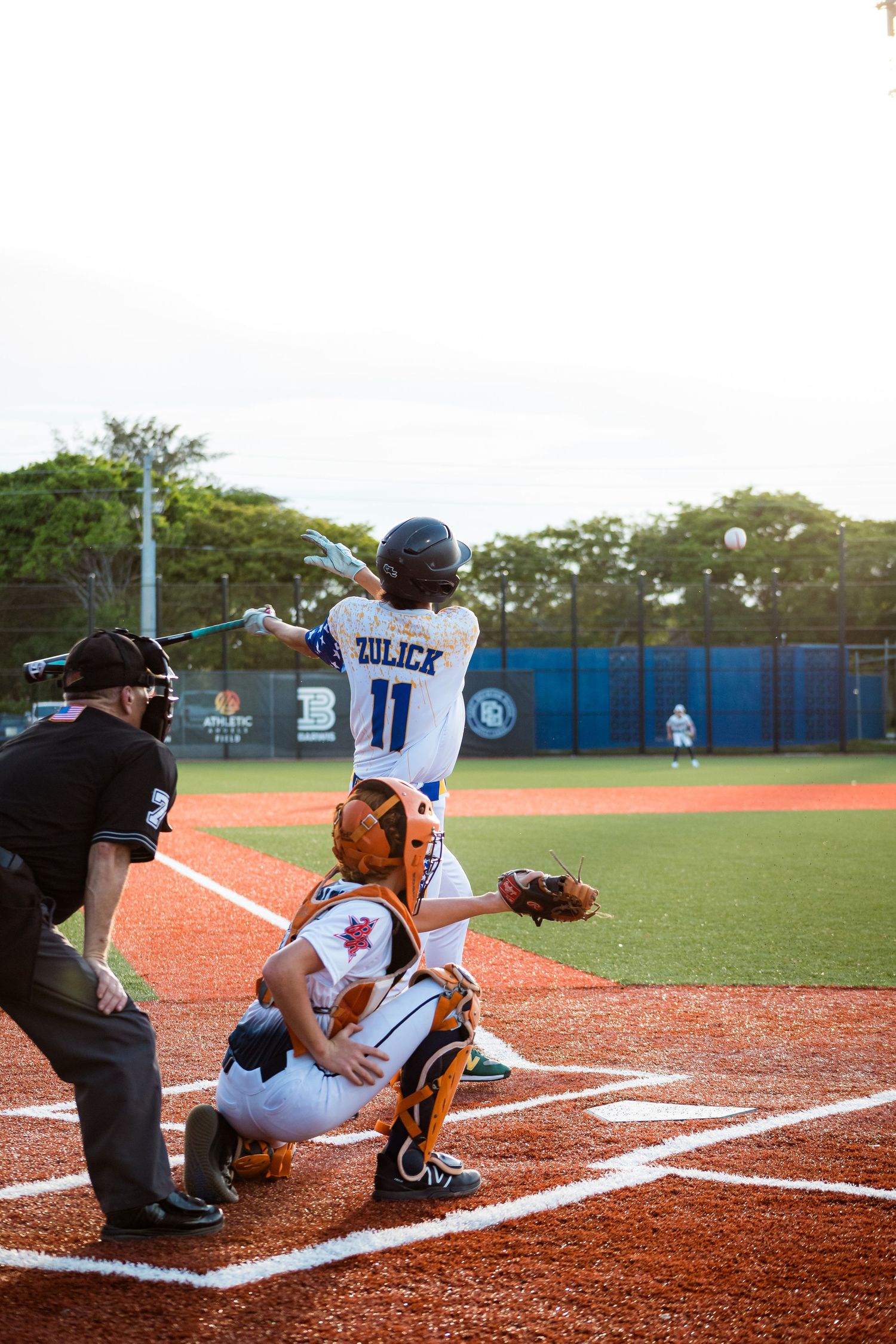 Baseball batter in uniform taking practice swings at home plate while catcher and umpire get into position.