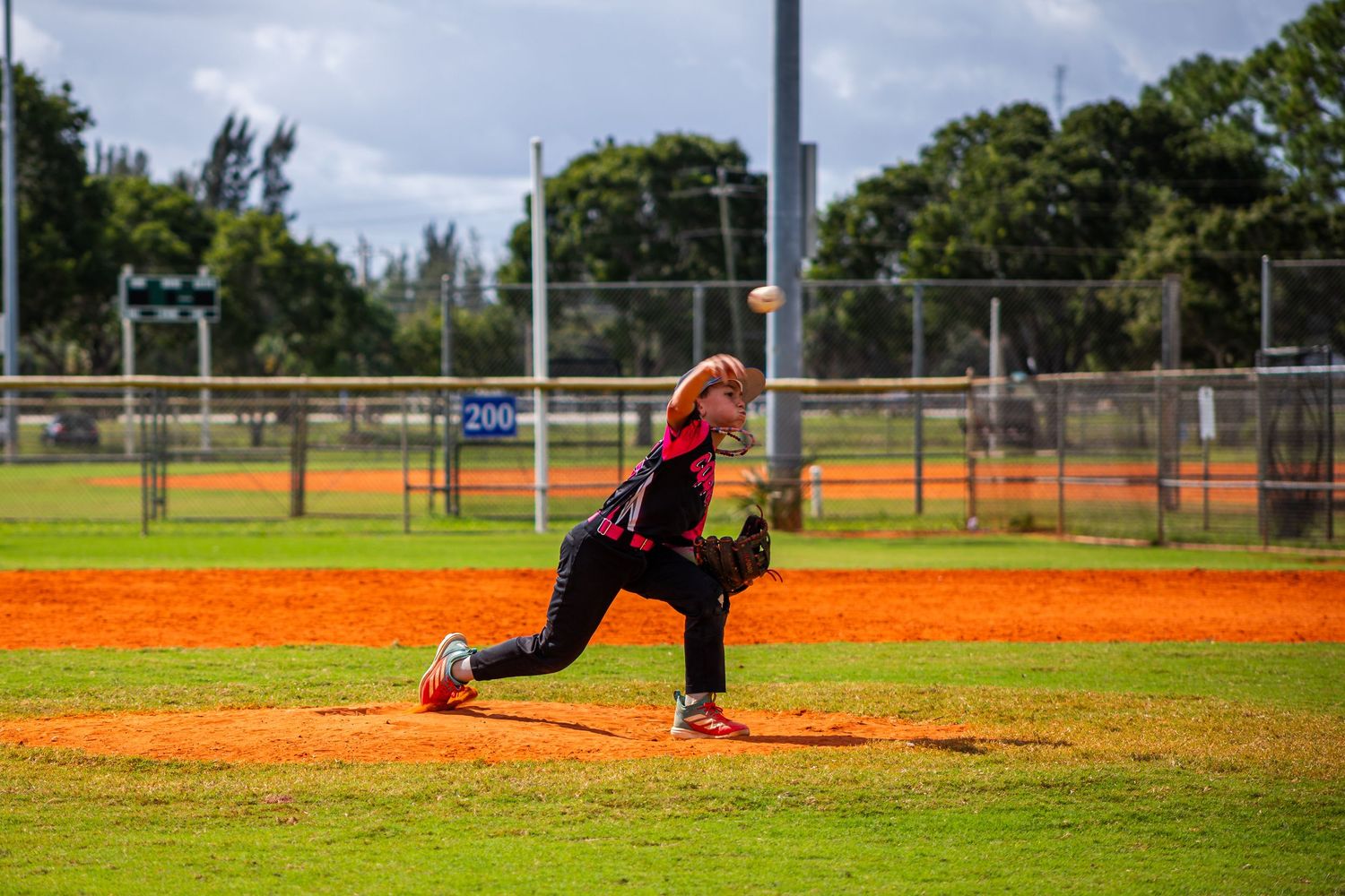 Baseball pitcher in mid-delivery motion on dirt mound during game at outdoor baseball field.