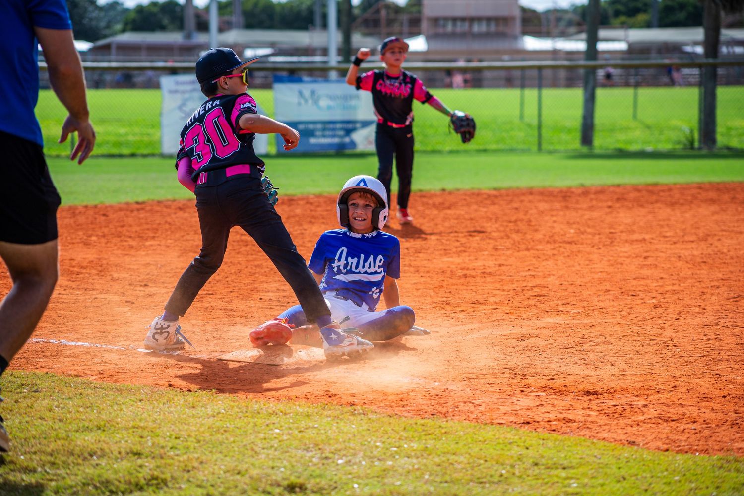 Baseball player slides into base as cloud of orange dirt kicks up during intense gameplay moment.