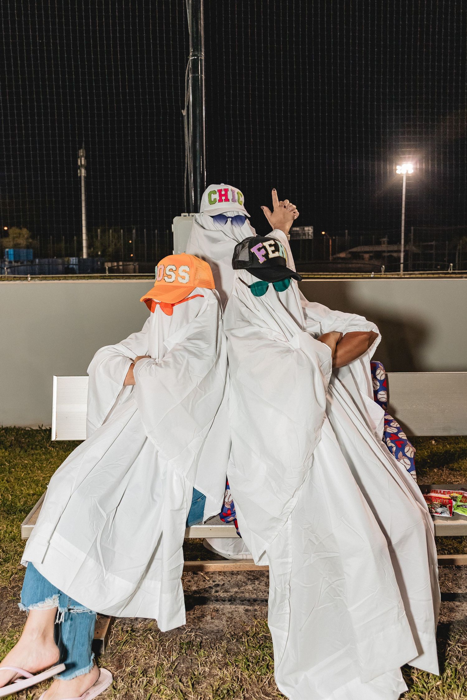 Group wearing white sheets and orange hats pose together at night on a sports field.