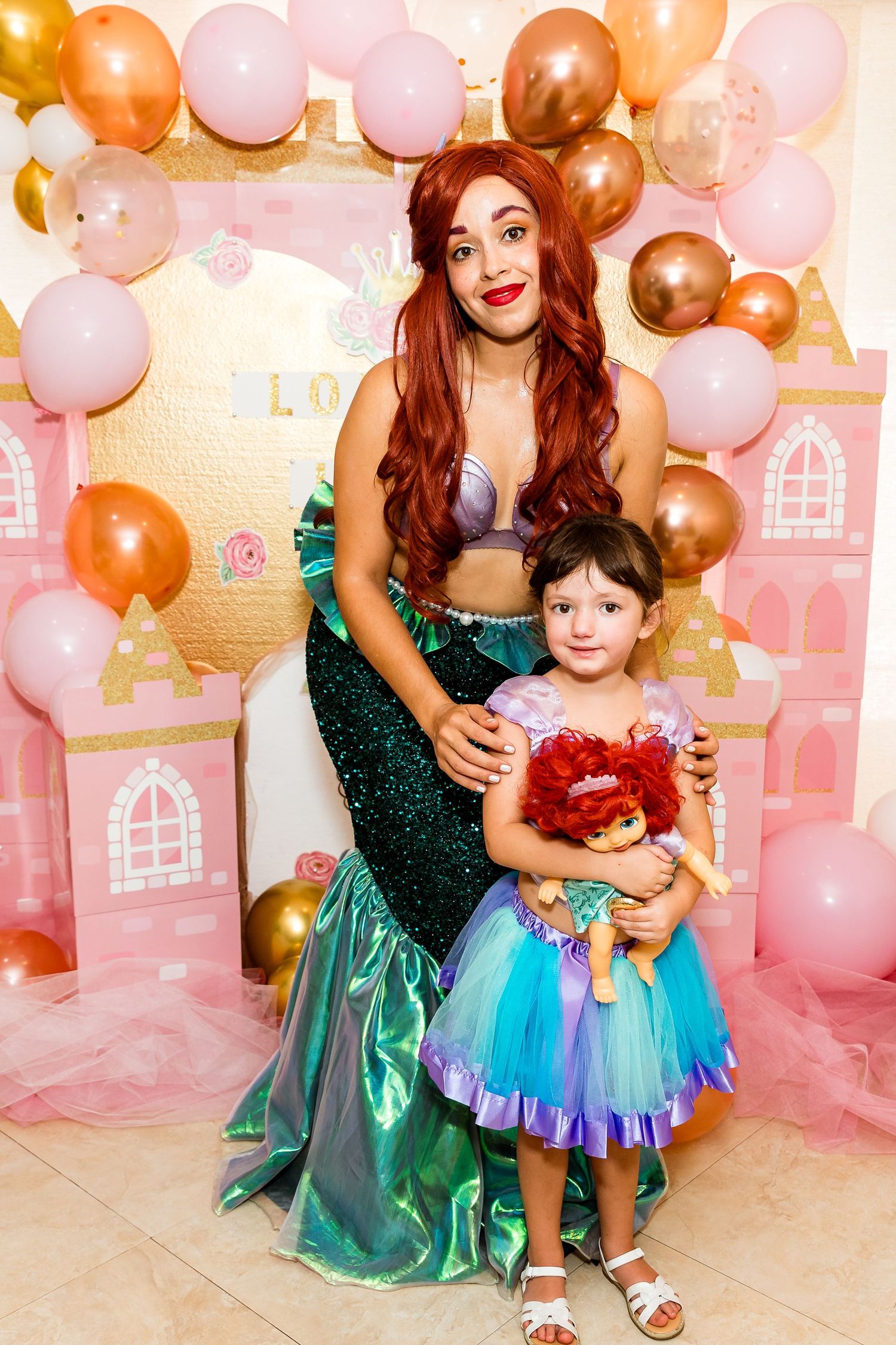 Princess party celebration with pink and gold balloon arch against a castle backdrop.
