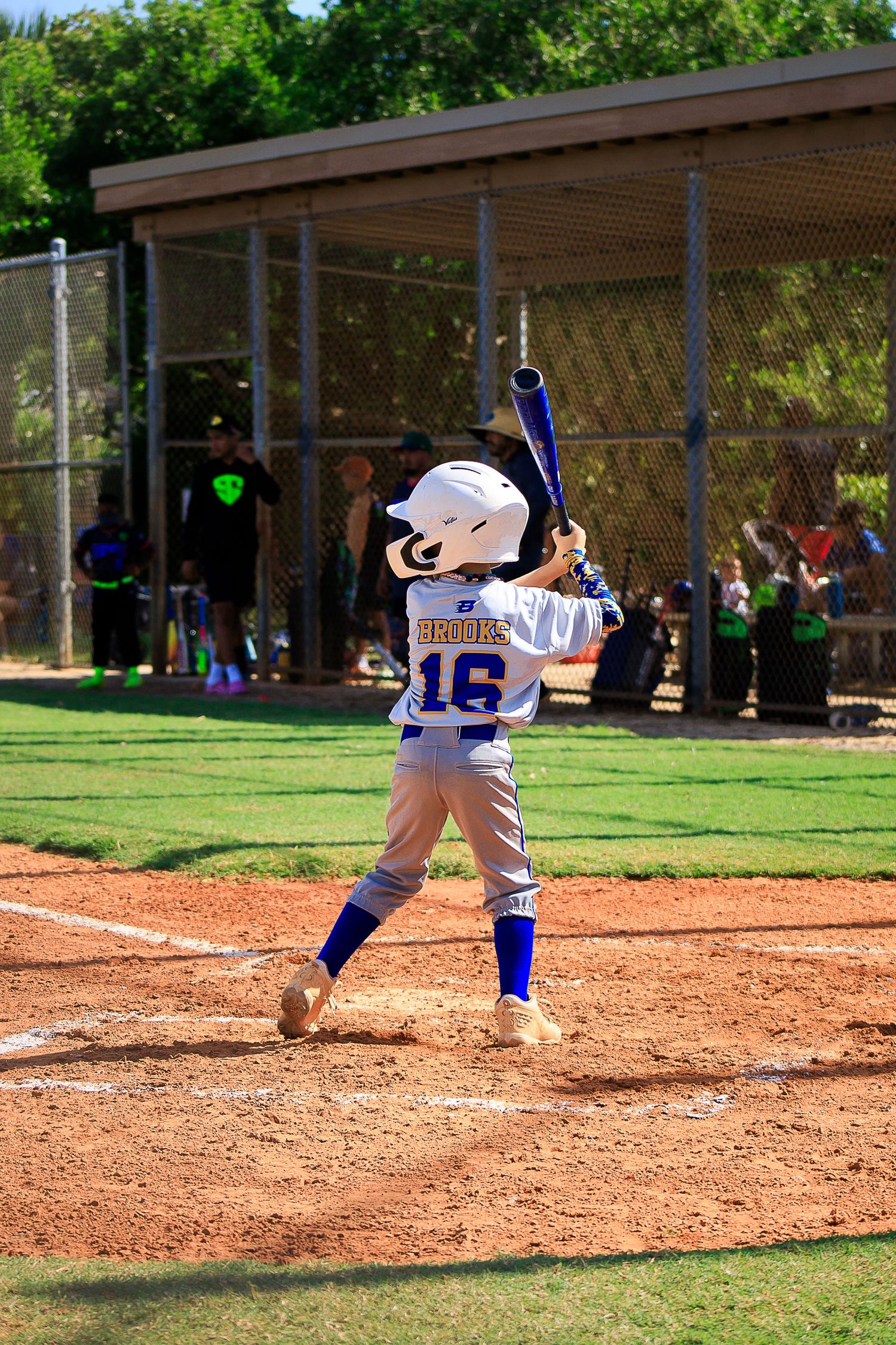 Youth batter in white uniform taking stance at home plate during baseball game.