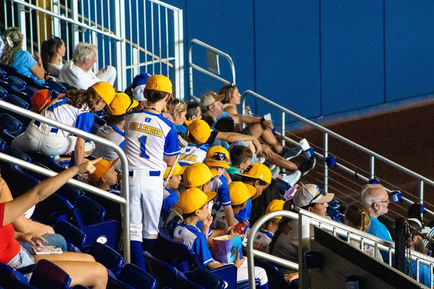 Spectators in yellow and blue uniforms watching game from stadium bleachers.